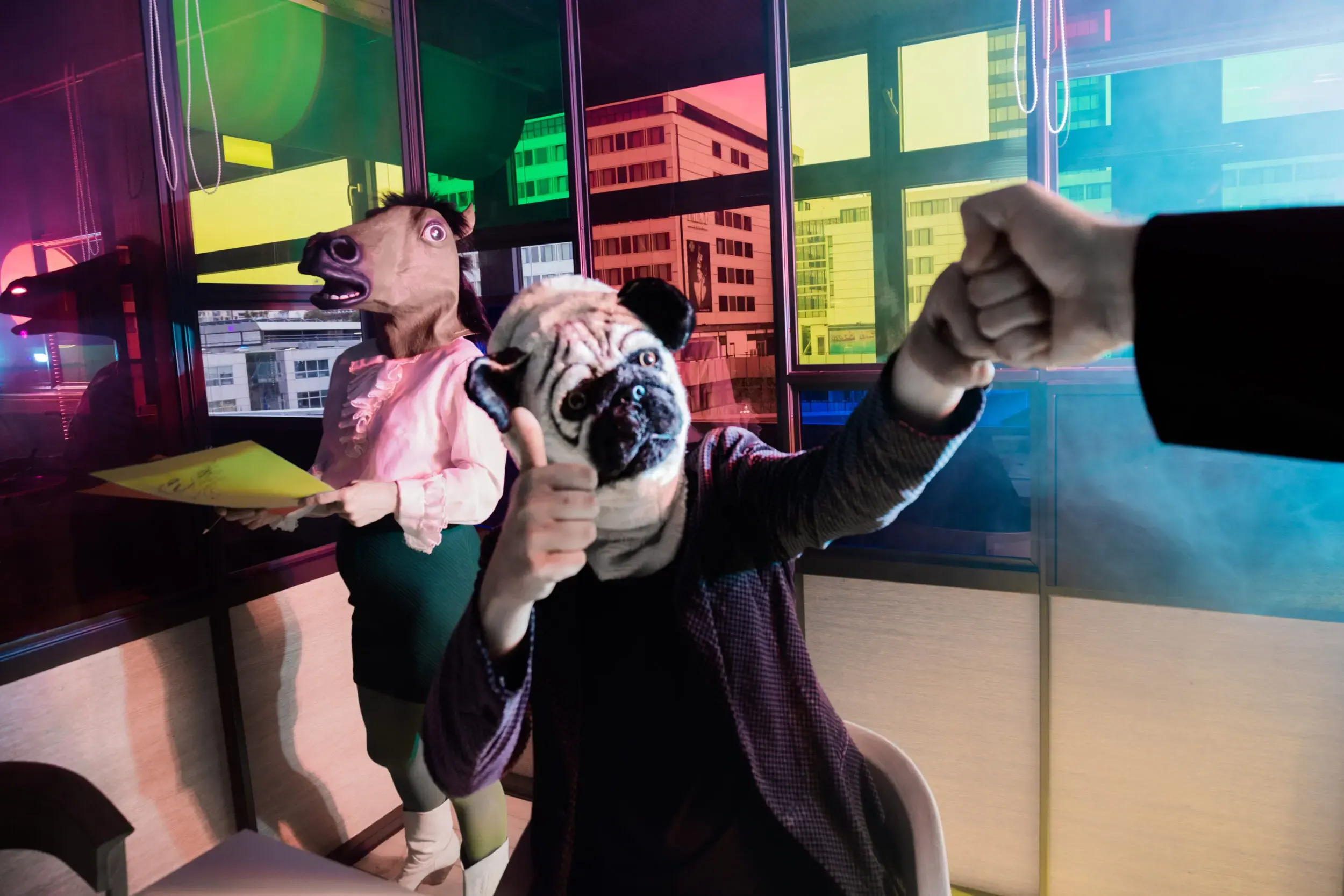 Costumed guests at an office desk, one pointing a phone at the camera under green lighting.