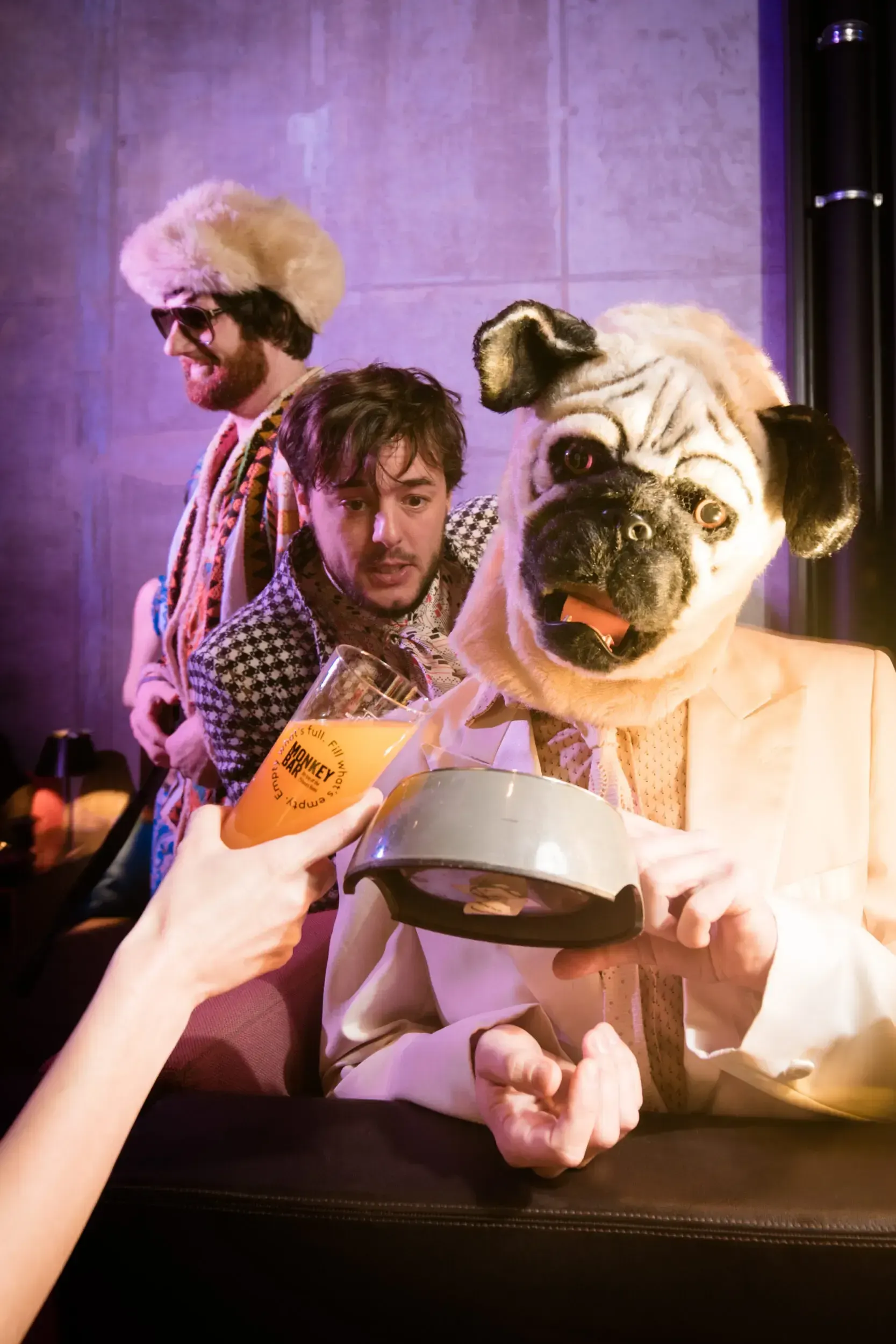 Guest pouring a drink into a metal bowl held by a person in a pug mask.