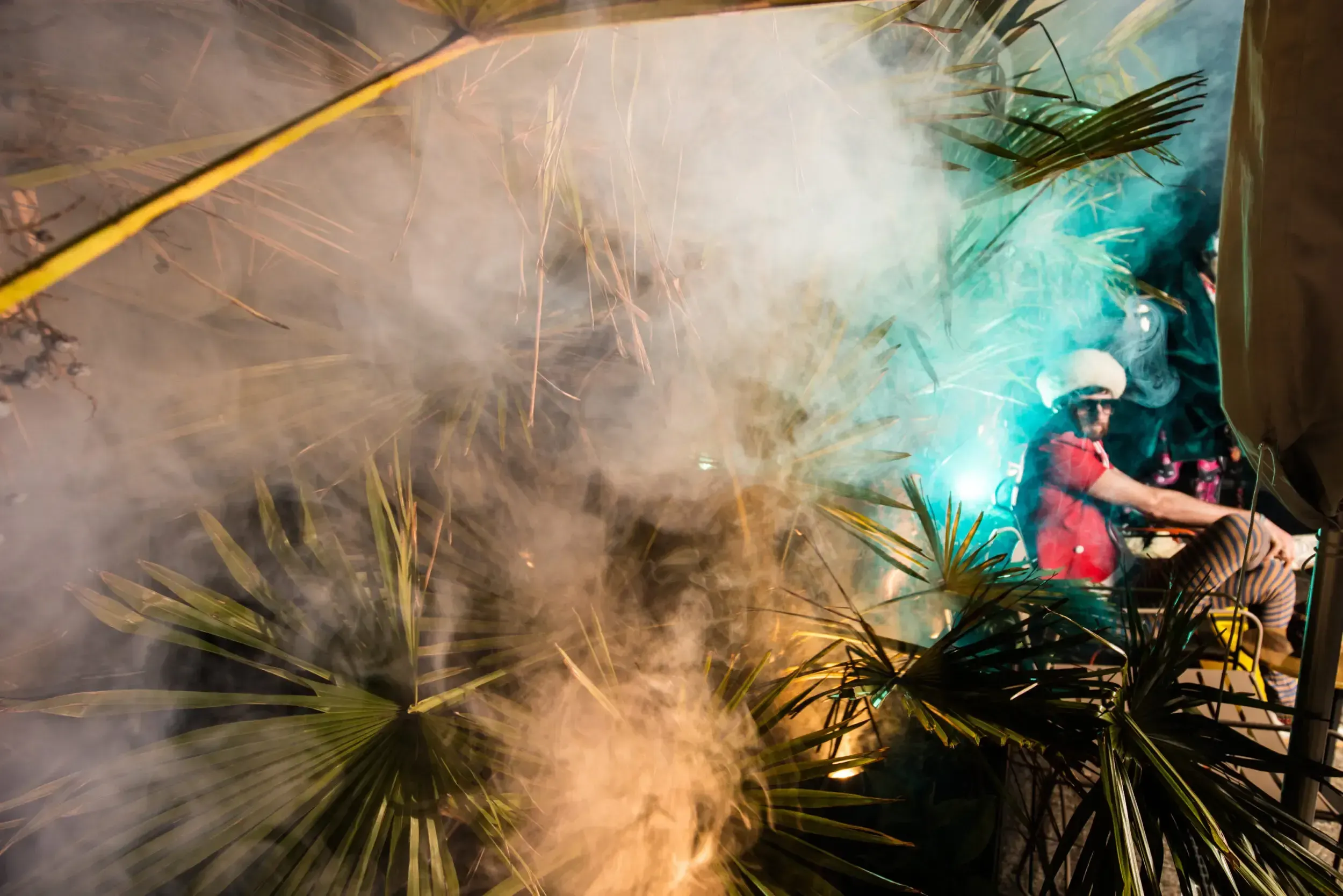 Costumed guest silhouetted in coloured smoke and sparks on the terrace at night.