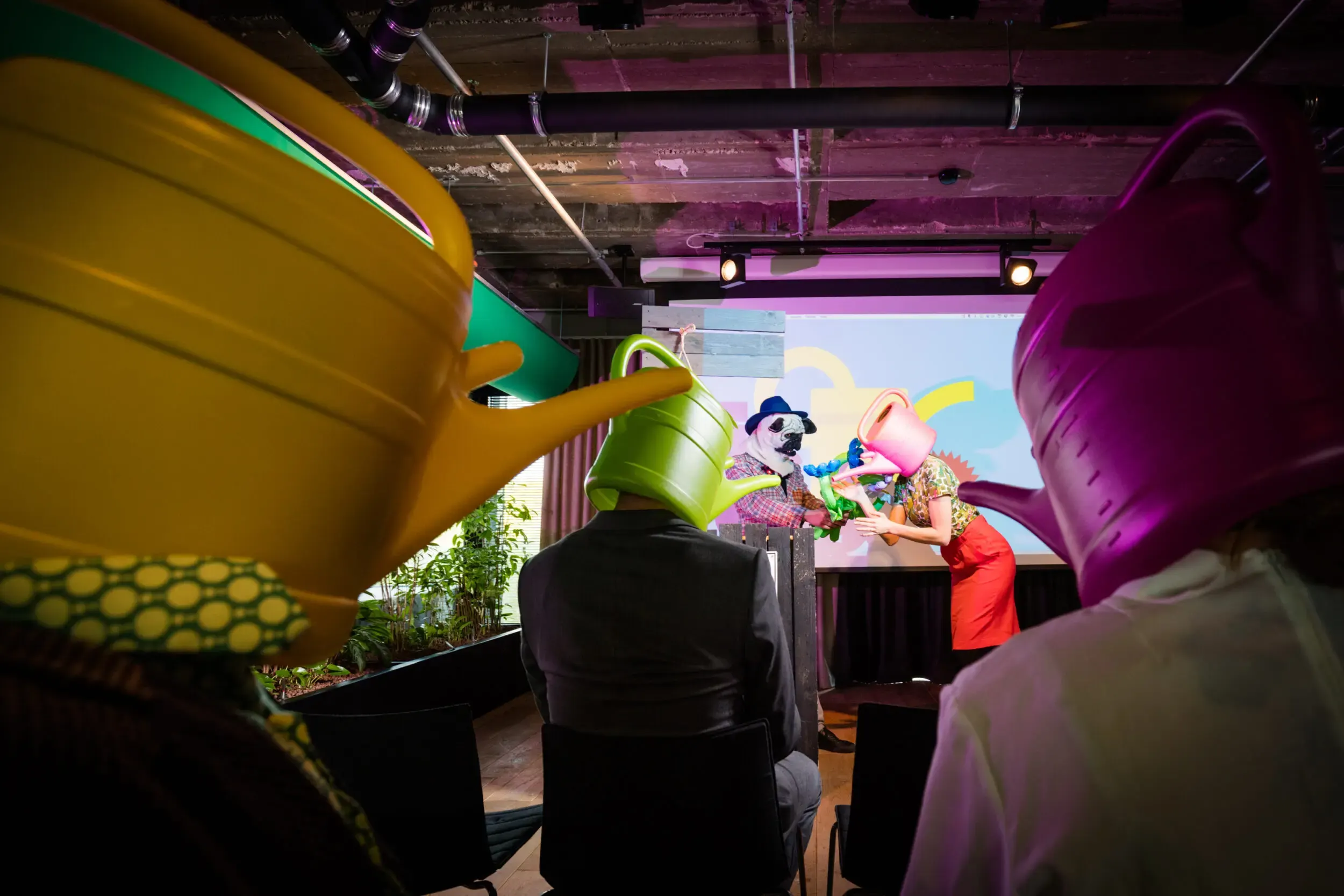 Guest in a yellow watering-can mask in a room decorated with inflatable balloon flowers.