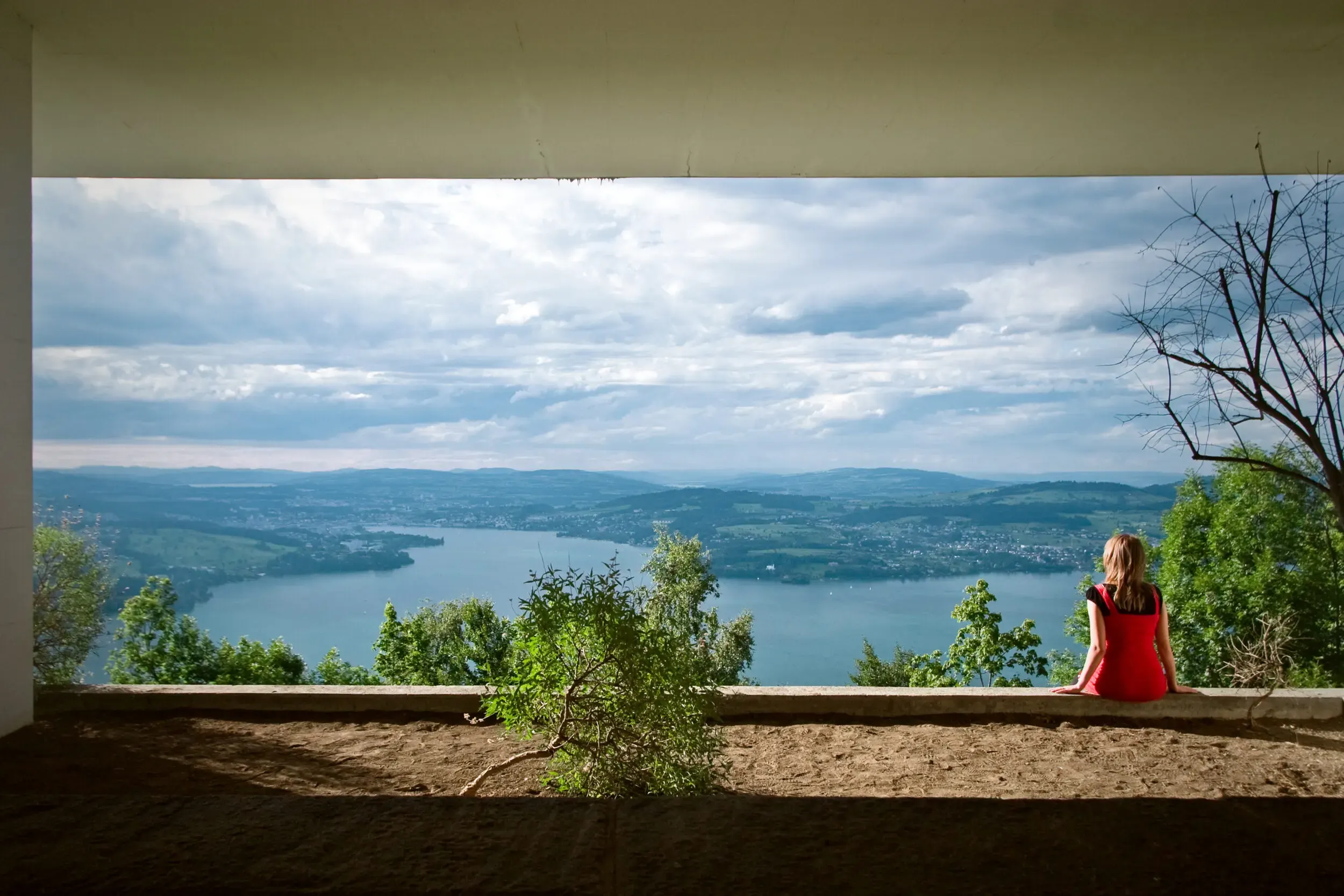 Person sitzt auf einer Mauer mit Blick auf einen See, Cross Section