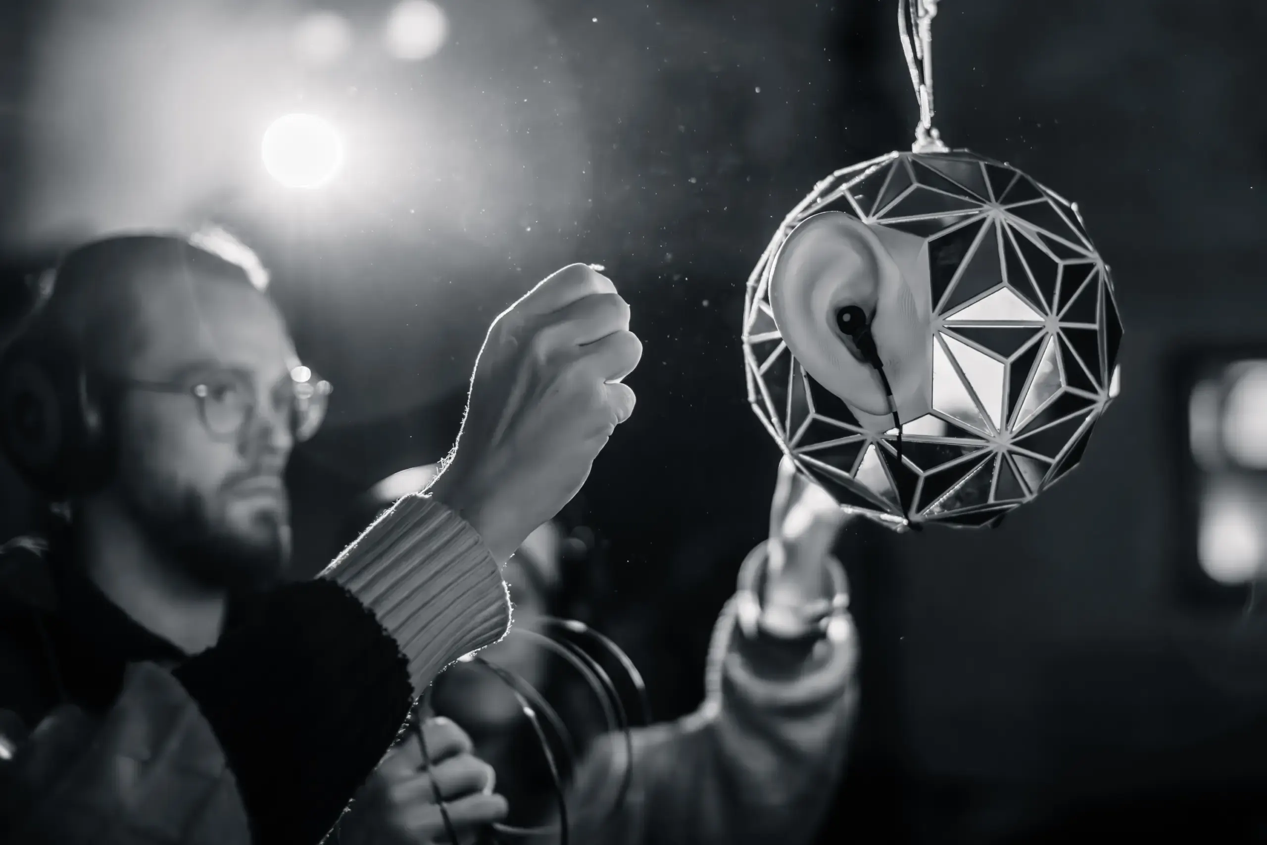 Schwarzweissfoto: Hand greift nach einer hängenden geometrischen Klangskulptur, Eigenklang