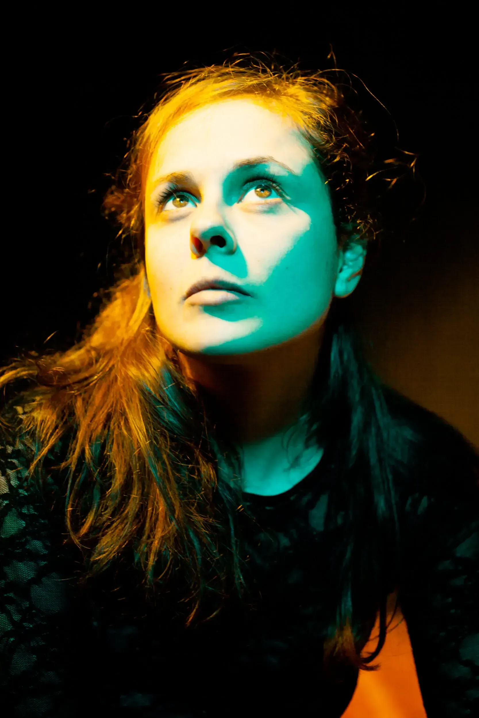 Portrait of Elisa Plüss looking upward, lit in warm orange and teal light.