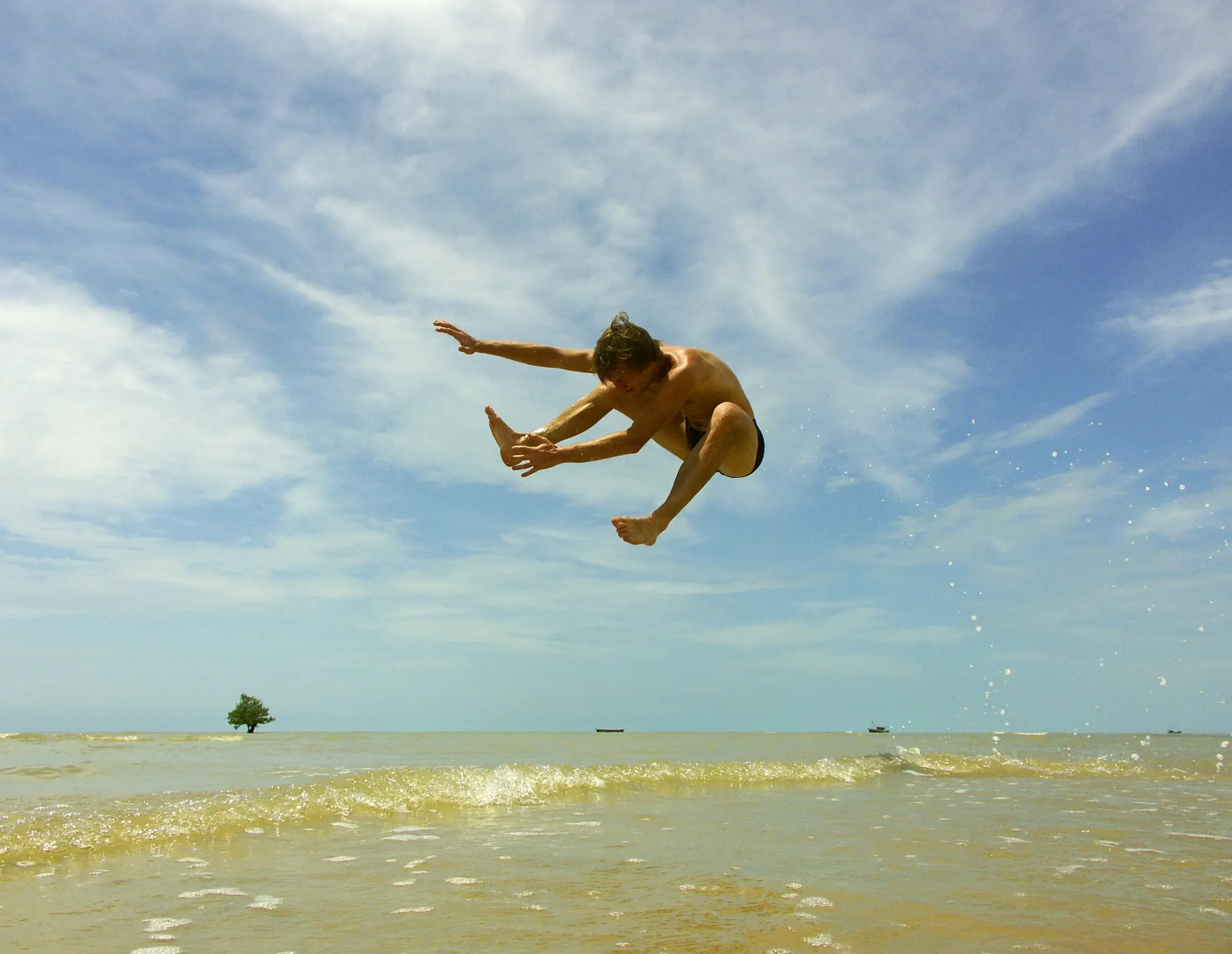 Person macht einen Salto am Strand unter bewölktem Himmel