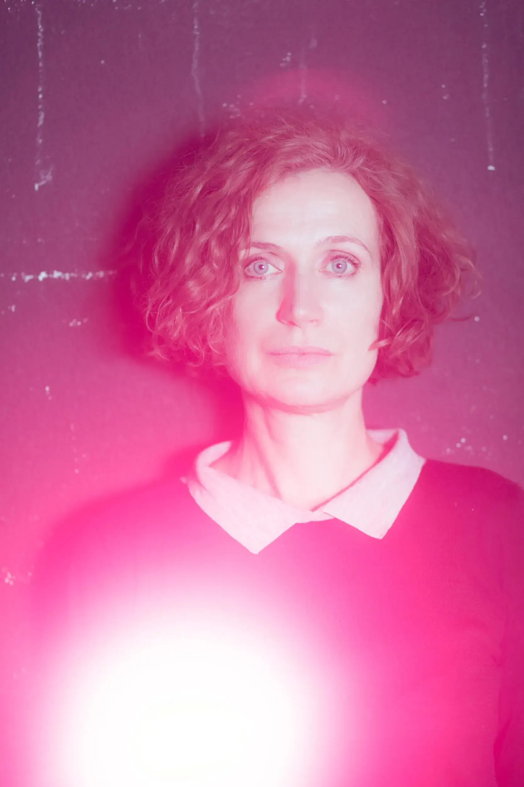 Portrait of Friederike Wagner bathed in intense magenta light against a textured wall.