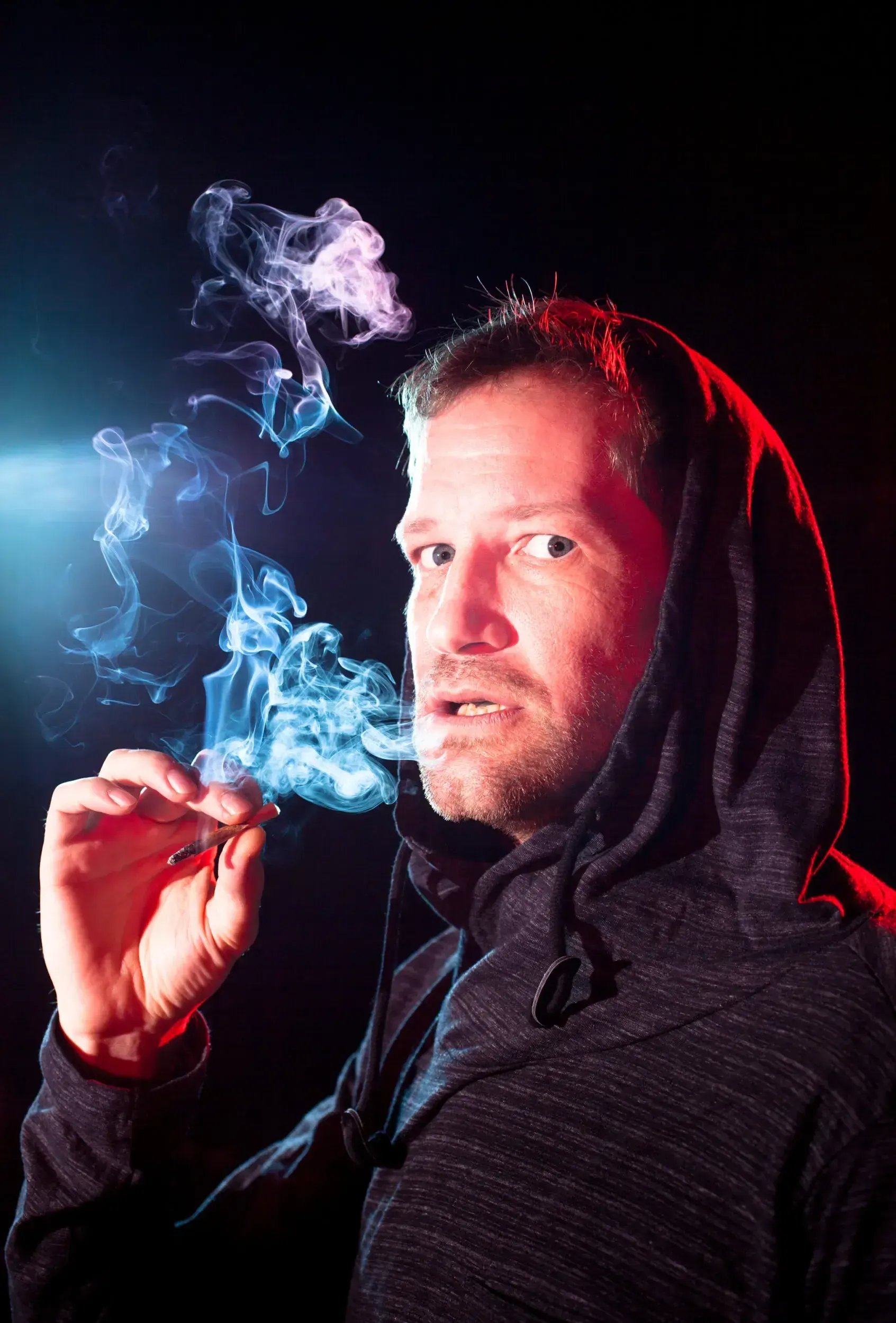 Portrait of Fritz Fenne in a hoodie smoking a cigarette, lit in red and blue.