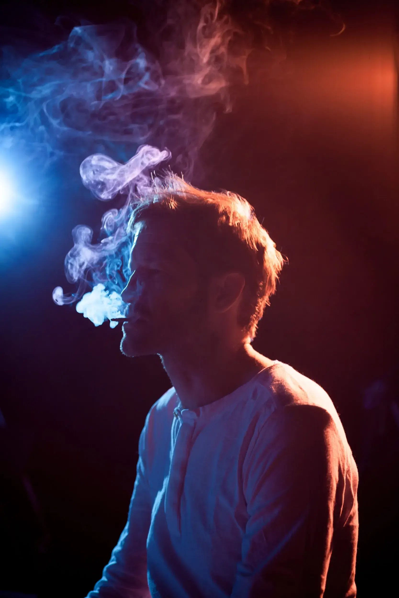 Profile portrait of Fritz Fenne exhaling smoke, lit in blue and orange.