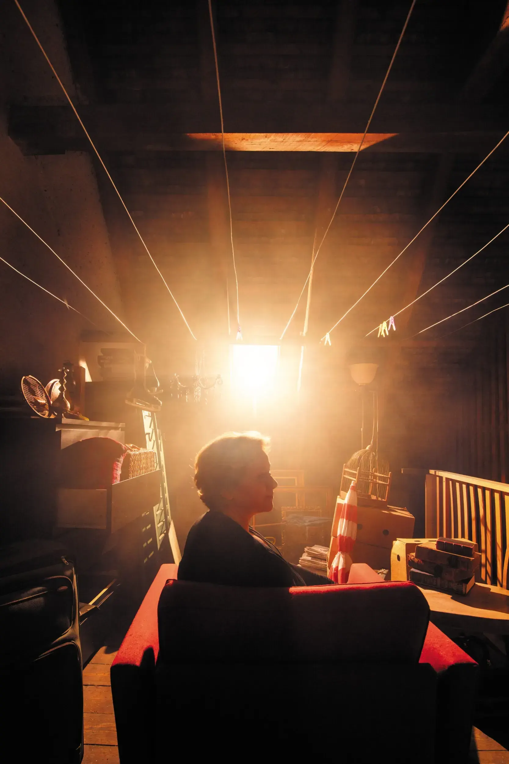 Woman sitting in a sunlit cluttered attic room, the full-frame source image for the 'Glückliche Tage' poster.