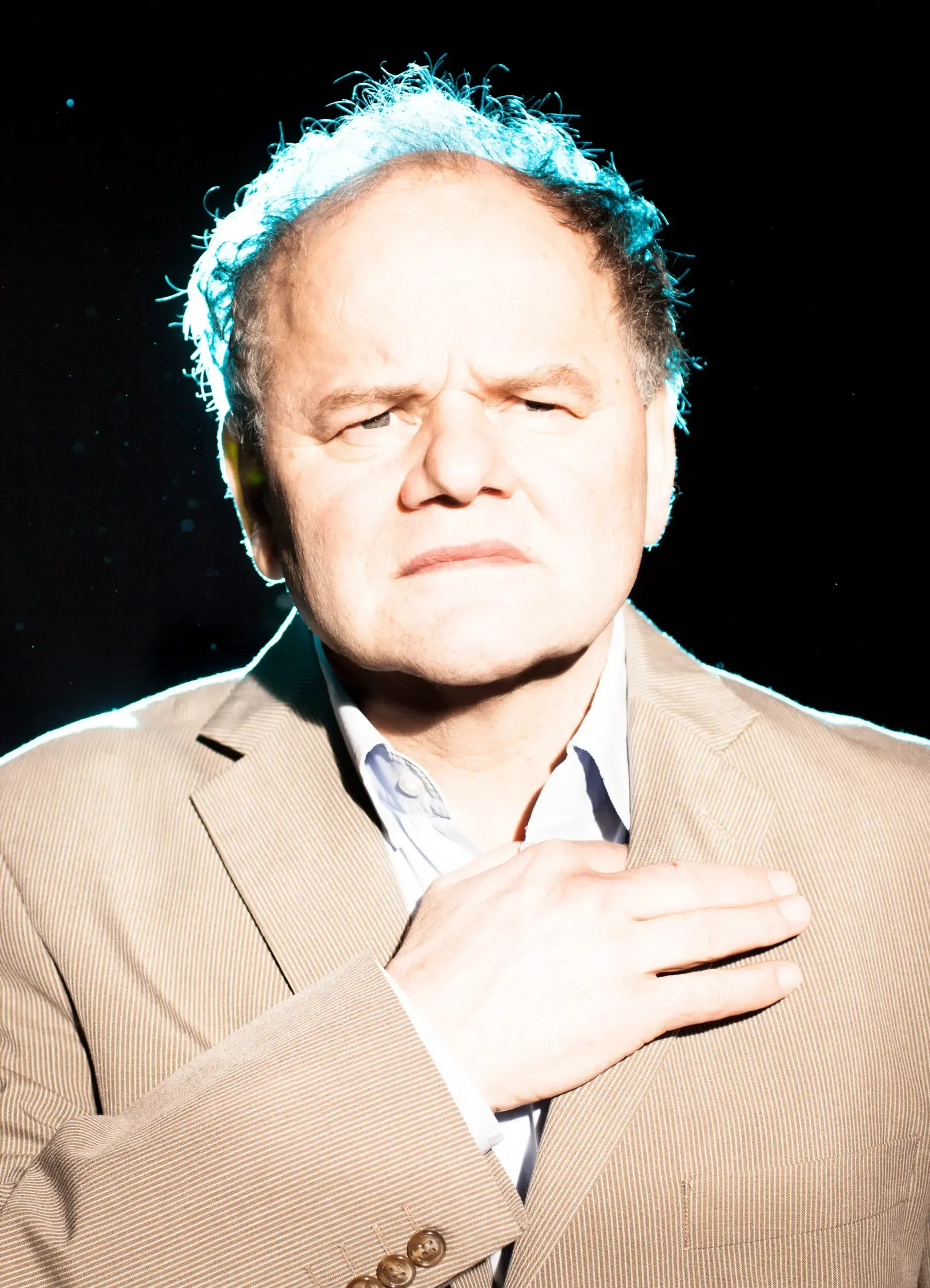 Portrait of Gottfried Breitfuss with a glowing teal outline, hand on chest, against a black background.