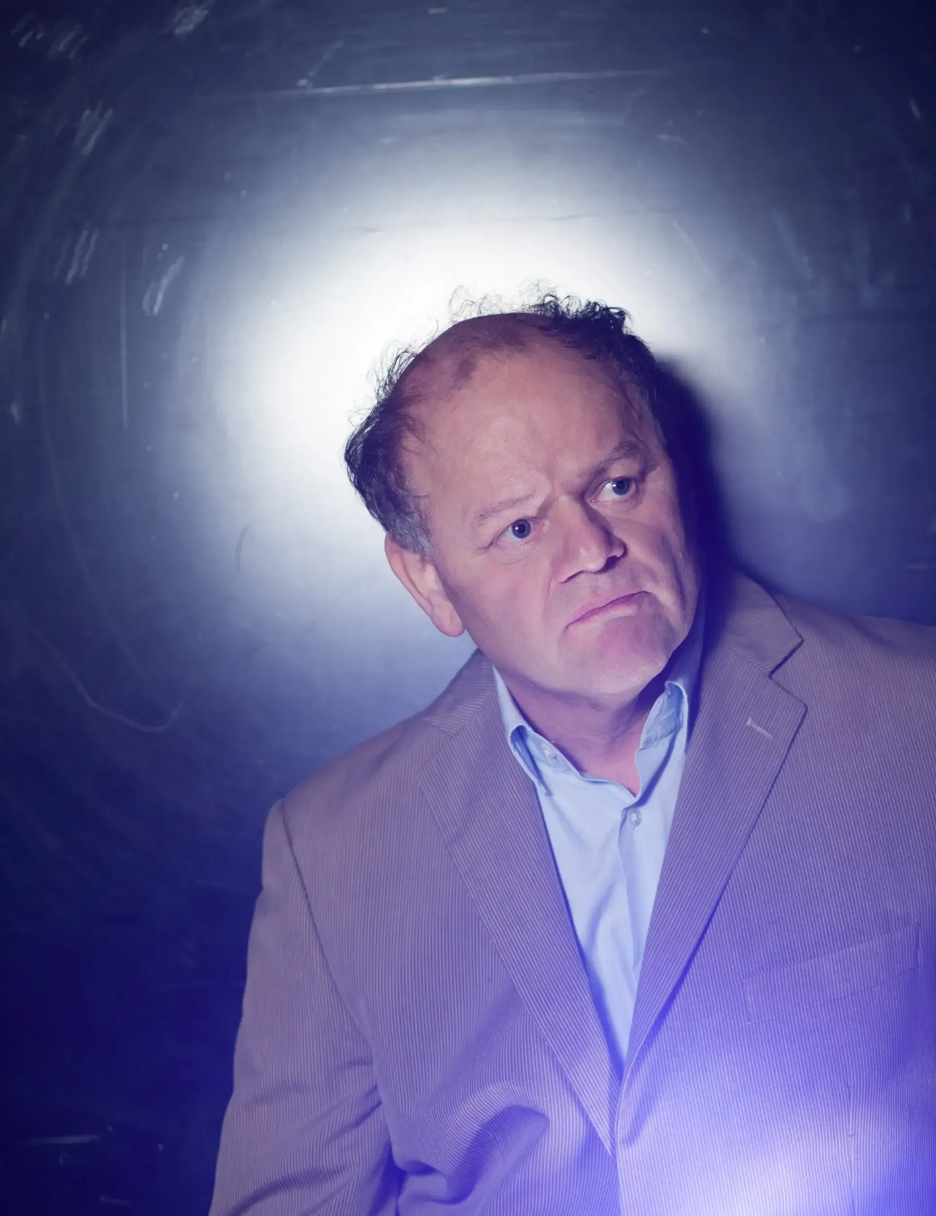 Portrait of Gottfried Breitfuss lit from behind by a purple glow against a dark wall.