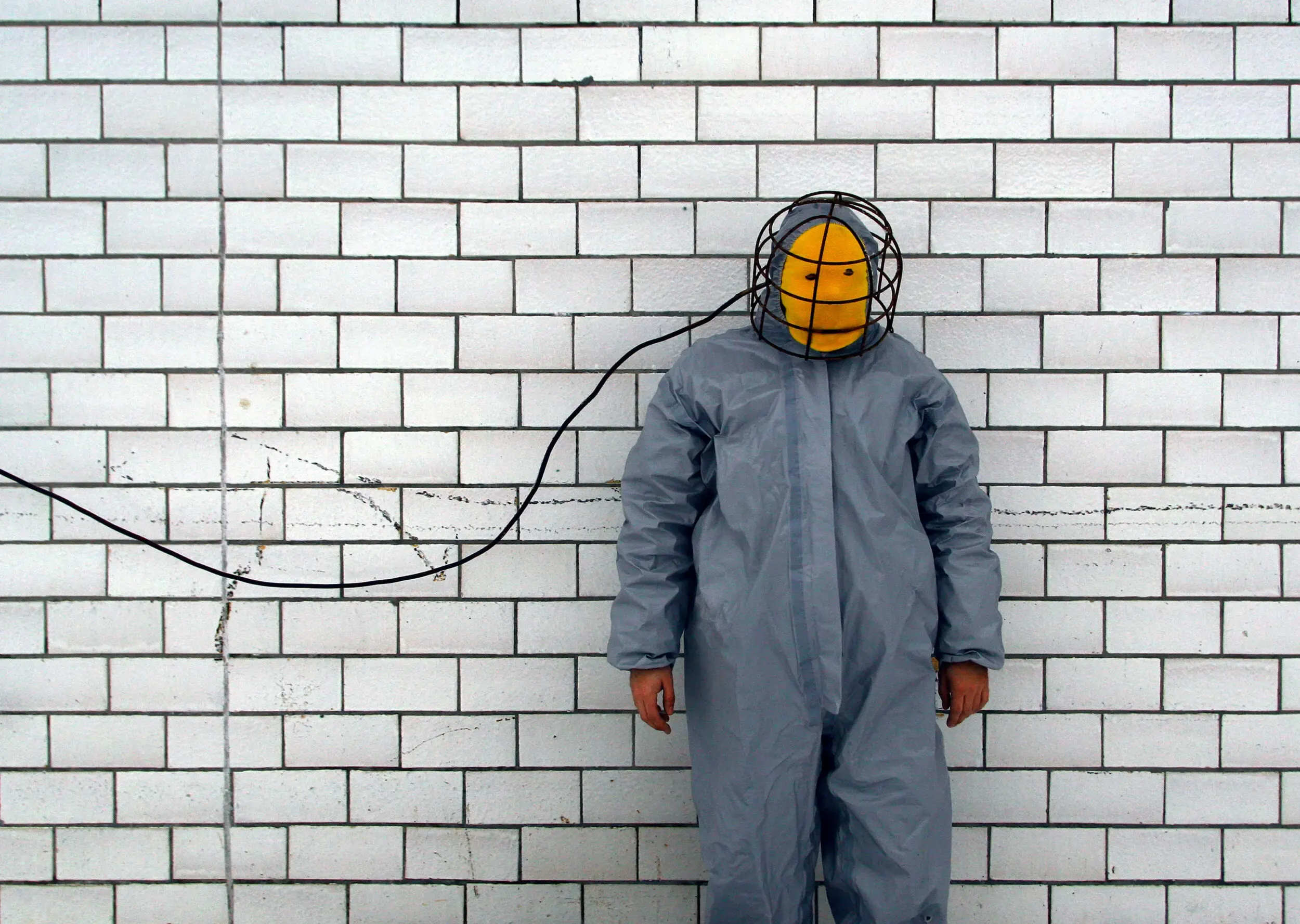 Person im Schutzanzug an weisser Backsteinwand mit Kabel am Helm, graugelb™