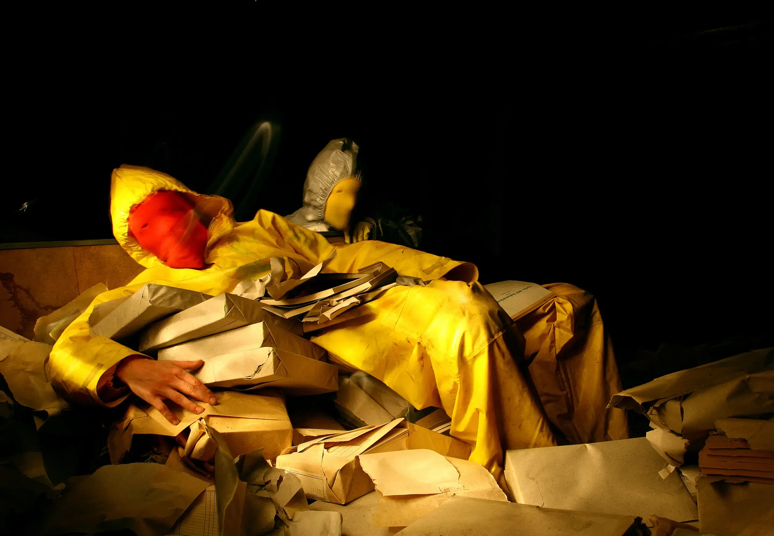 Person im Schutzanzug sitzt zwischen Kartonschachteln bei Nacht, graugelb™