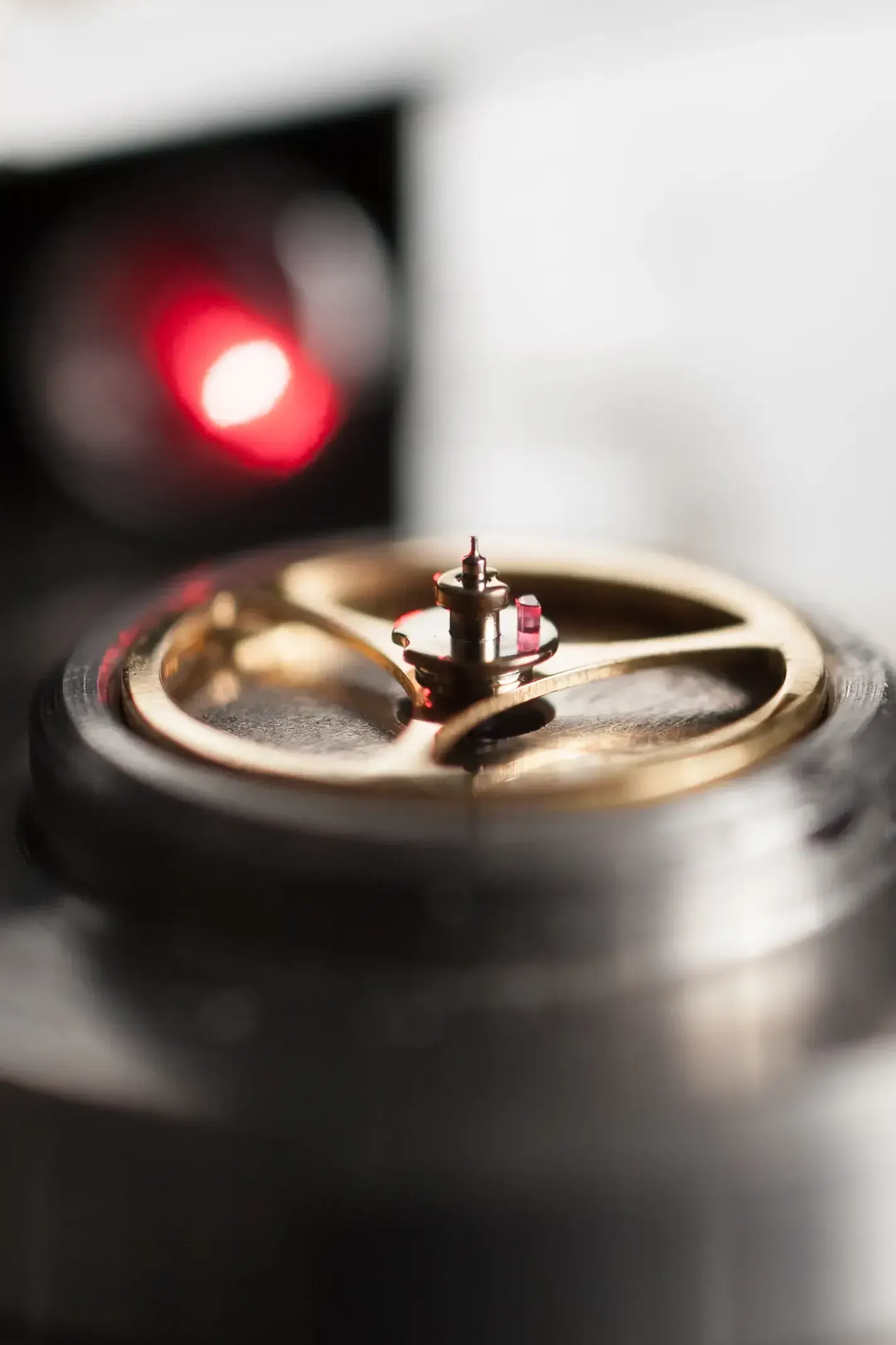 Extreme close-up of a golden watch balance wheel lit by a red measuring light at Greiner Vibrograf.