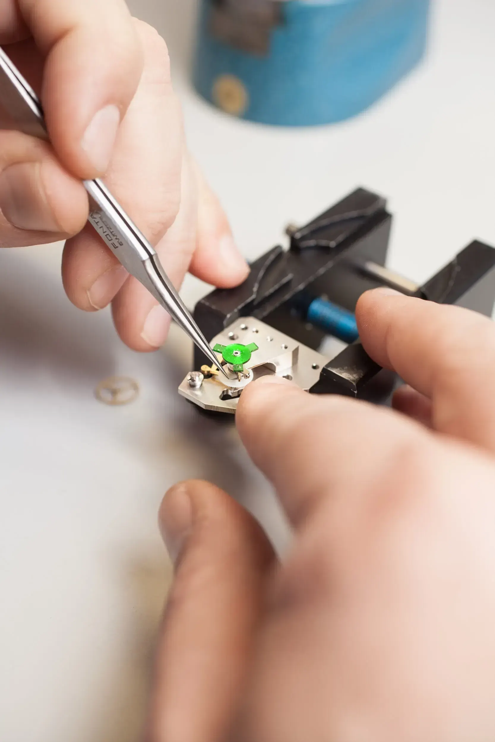Hands using tweezers to assemble a tiny green watch component at Greiner Vibrograf.