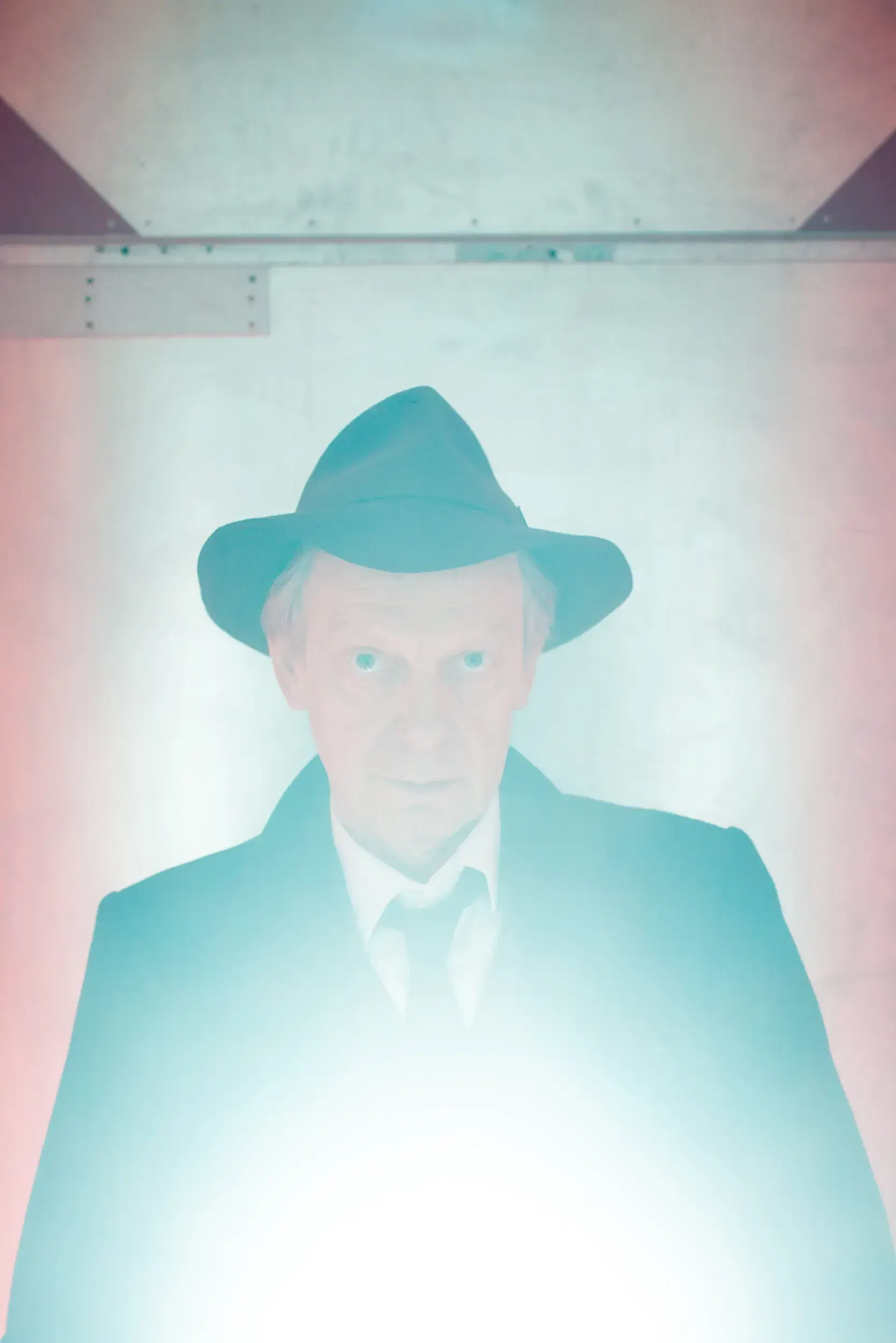 Portrait of actor Hans Kremer wearing a hat, glowing in pastel pink and teal light.