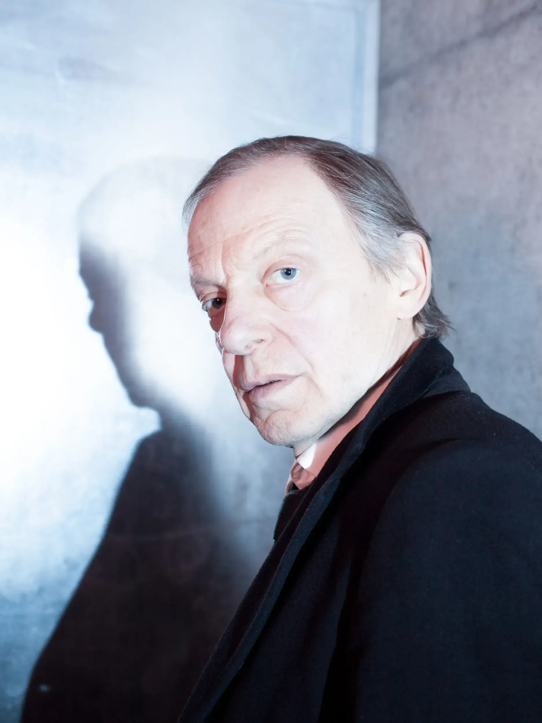 Portrait of actor Hans Kremer with his shadow cast on a lit wall behind him.
