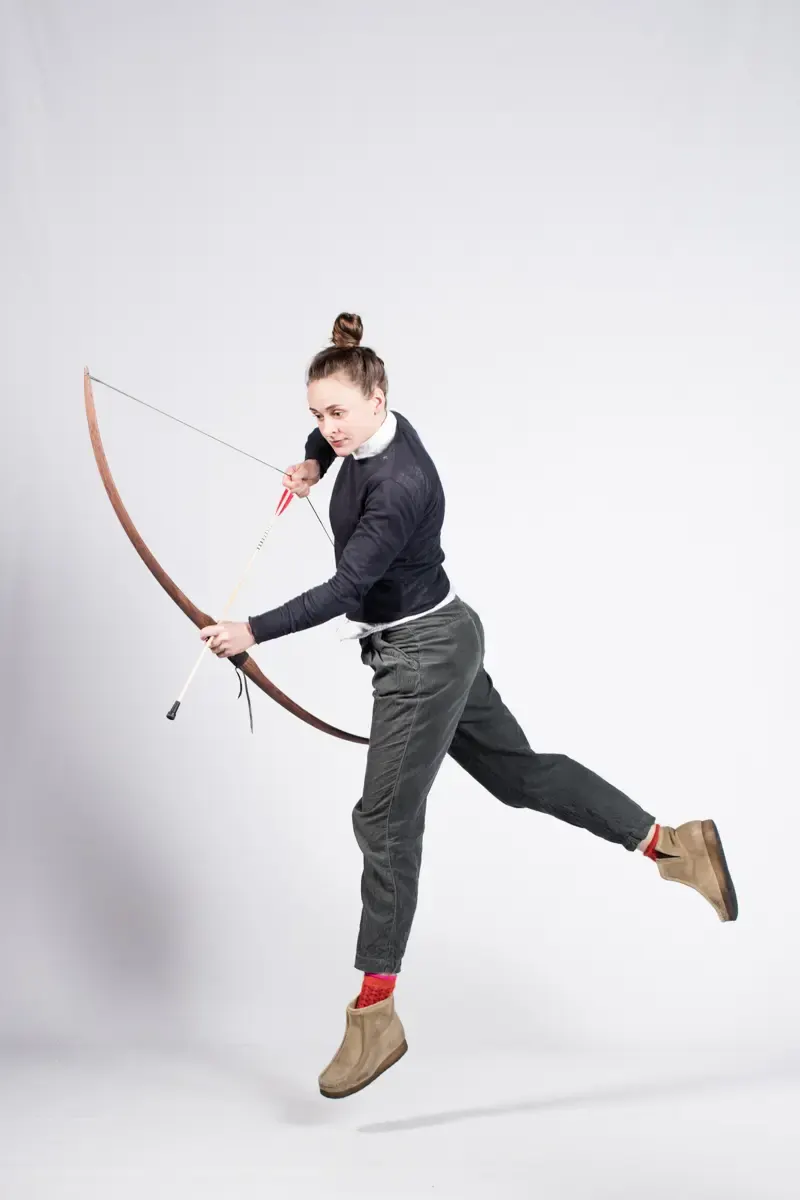 Henrike Johanna Jörissen balanciert mit Pfeil und Bogen auf einem Einrad vor weissem Hintergrund
