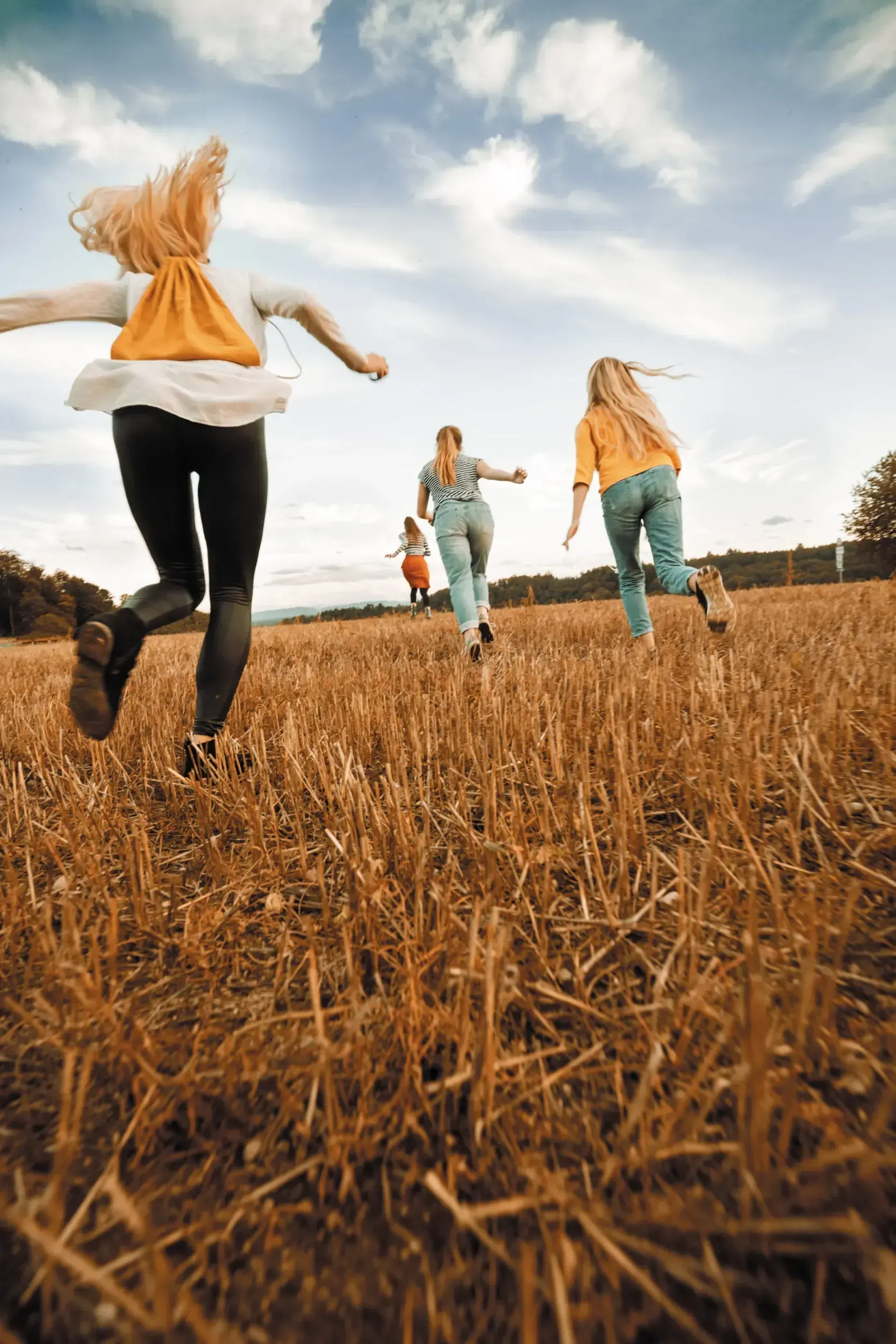 Four women running through a golden stubble field, the full-frame source image for the 'Hexenjagd' poster.