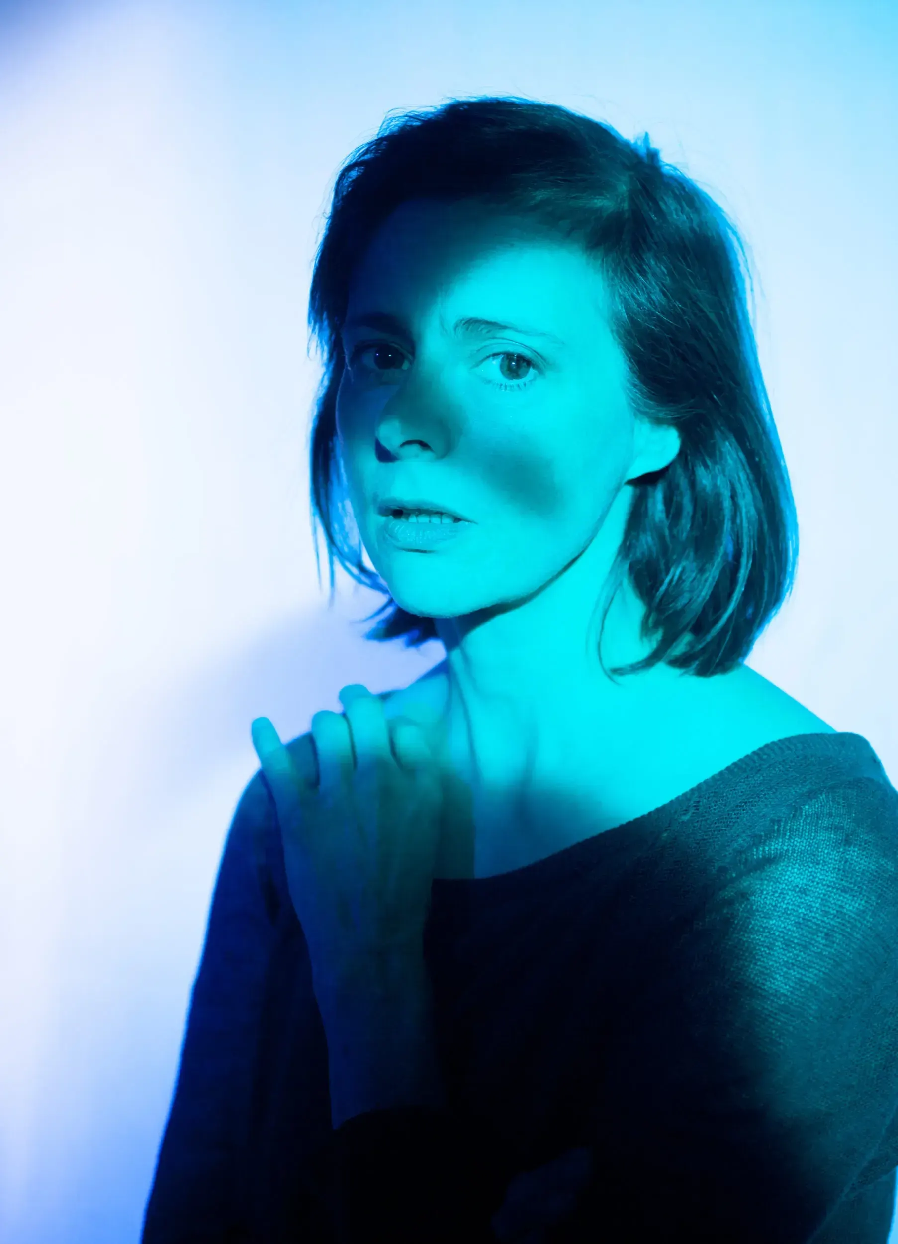 Portrait of actress Isabelle Menke lit entirely in cyan-blue light.