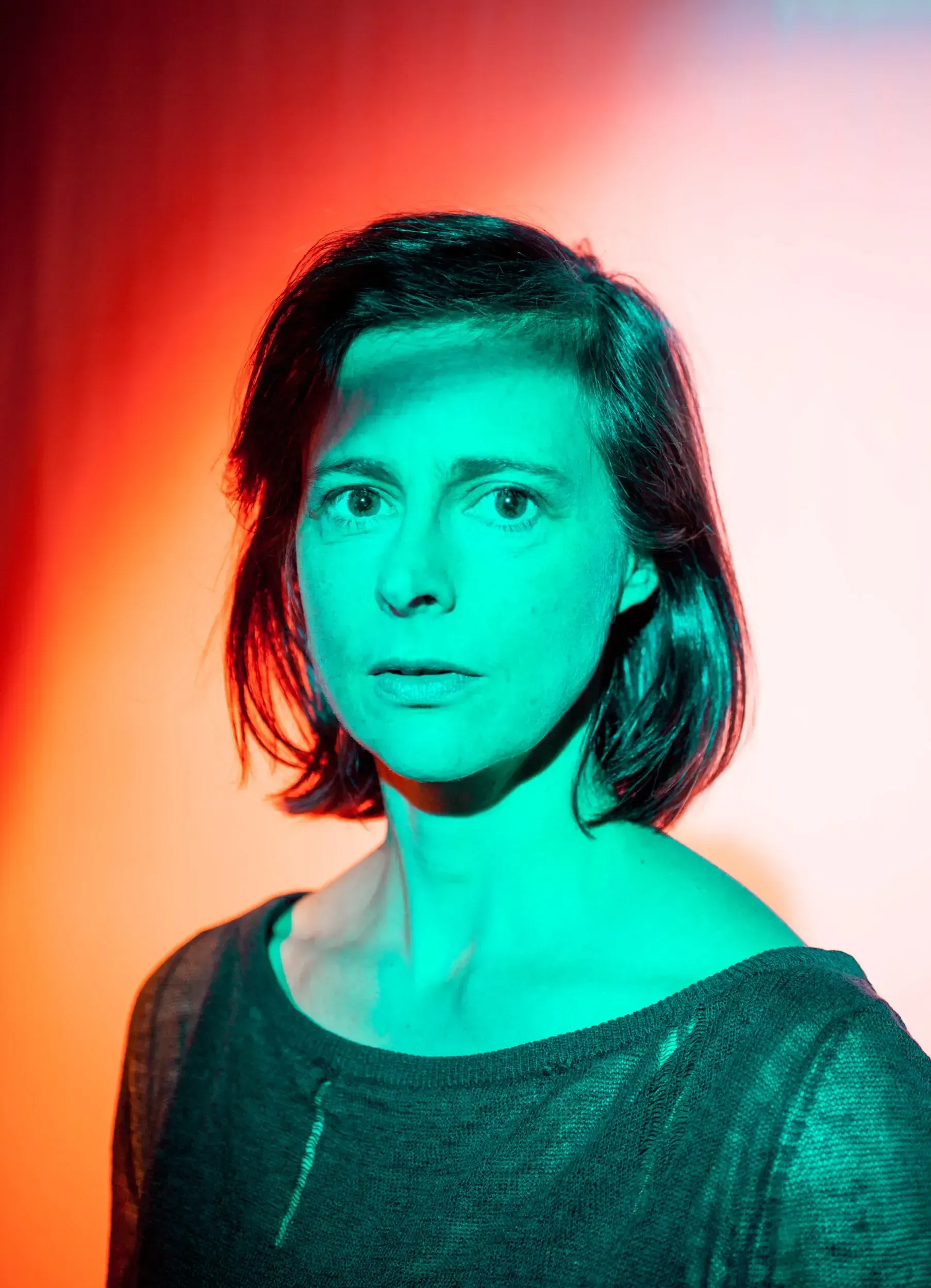 Portrait of actress Isabelle Menke lit in red and teal against a bright background.
