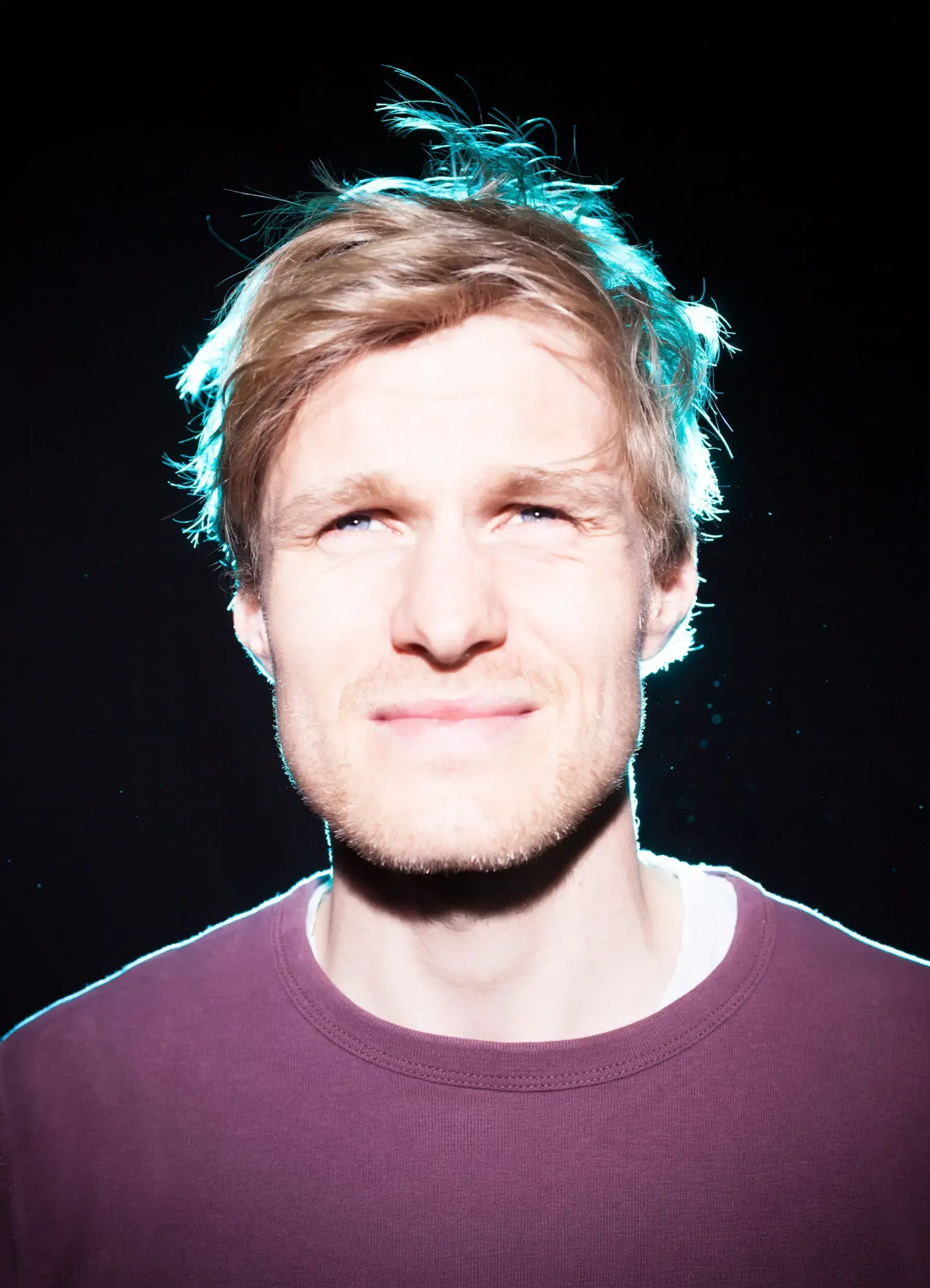 Portrait of actor Jirka Zett smiling, lit with a glowing teal outline against a black background.