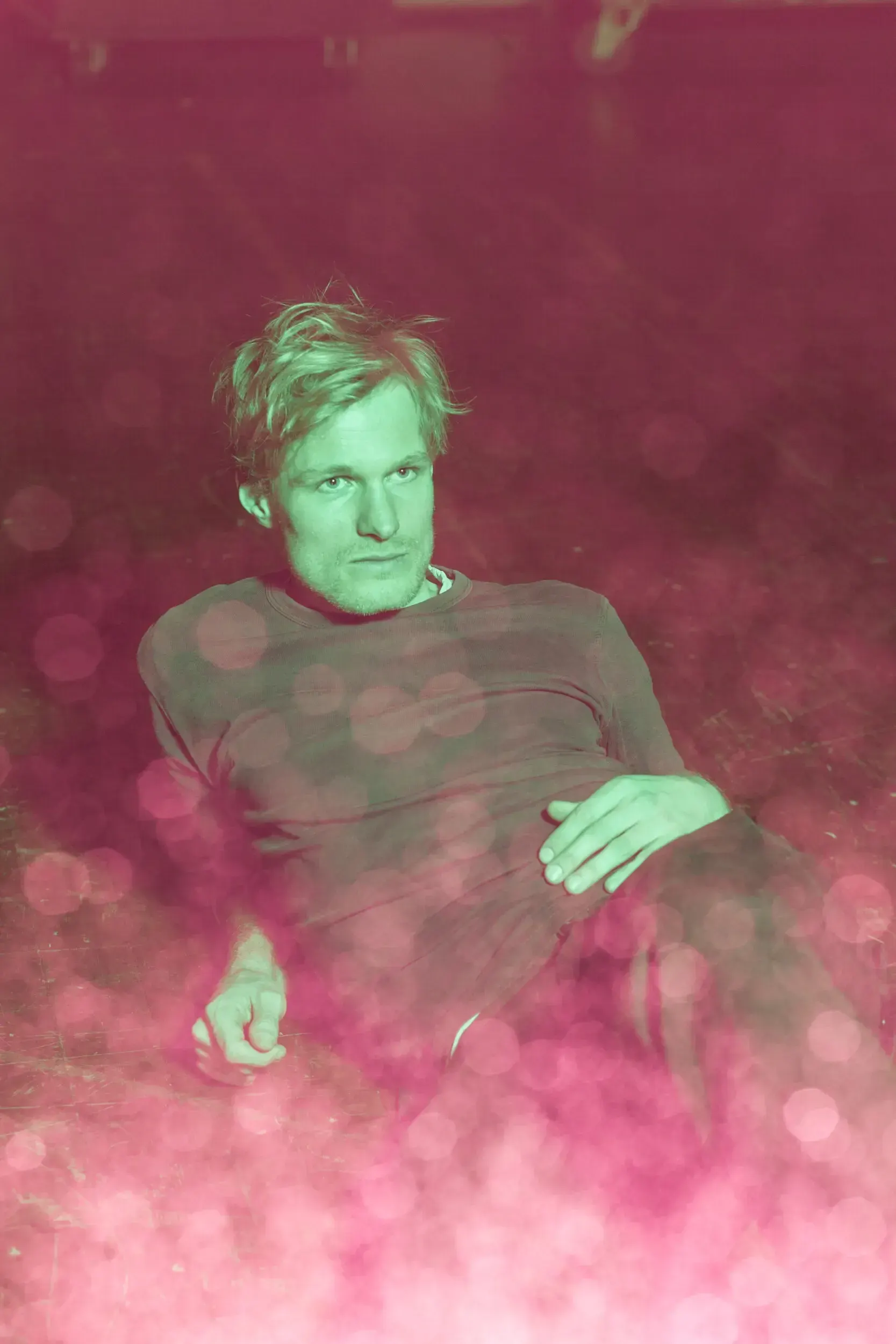Portrait of actor Jirka Zett reclining on the floor, lit in green and pink light.