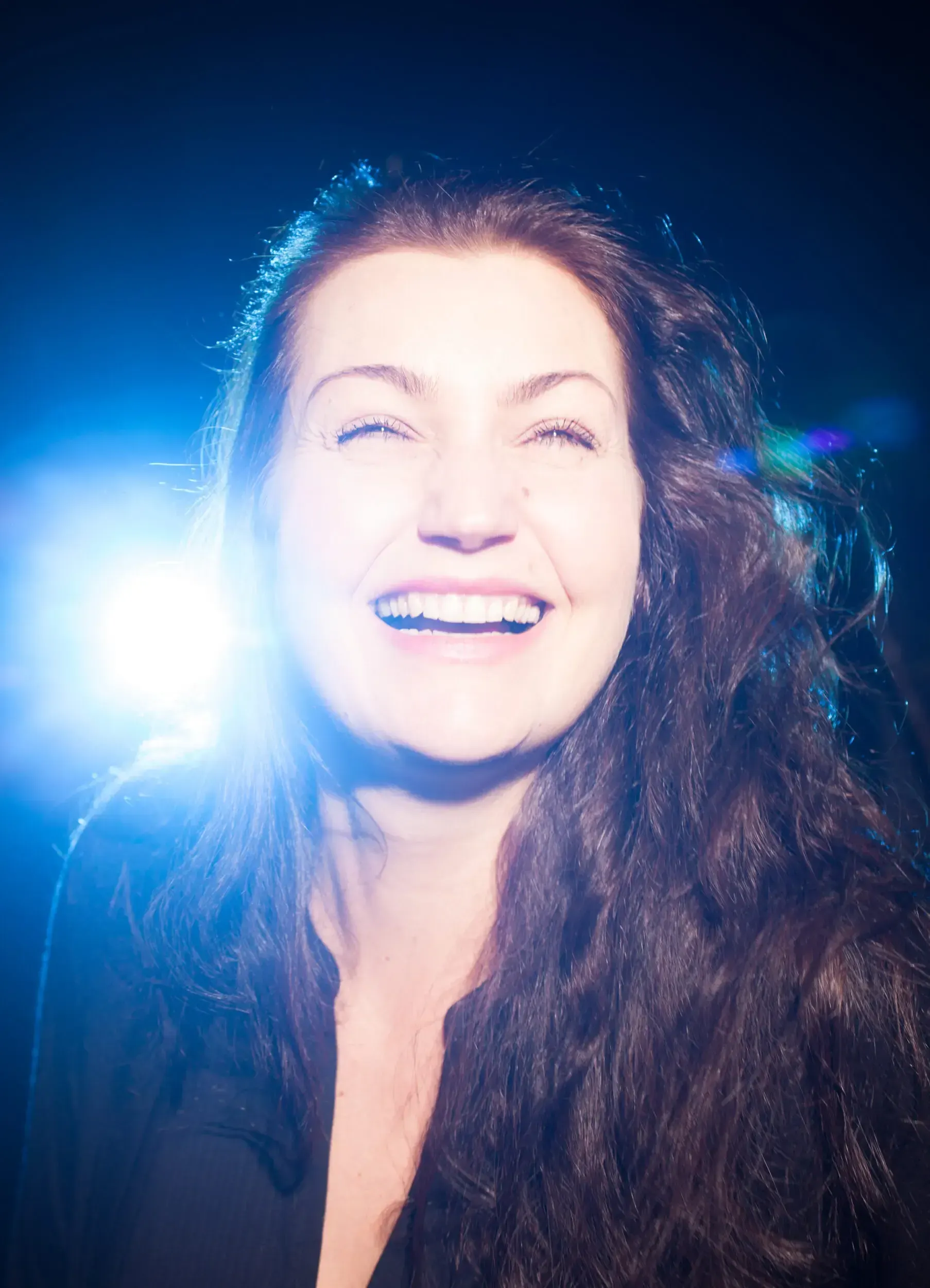 Portrait of actress Julia Kreusch laughing, backlit by a bright blue light.