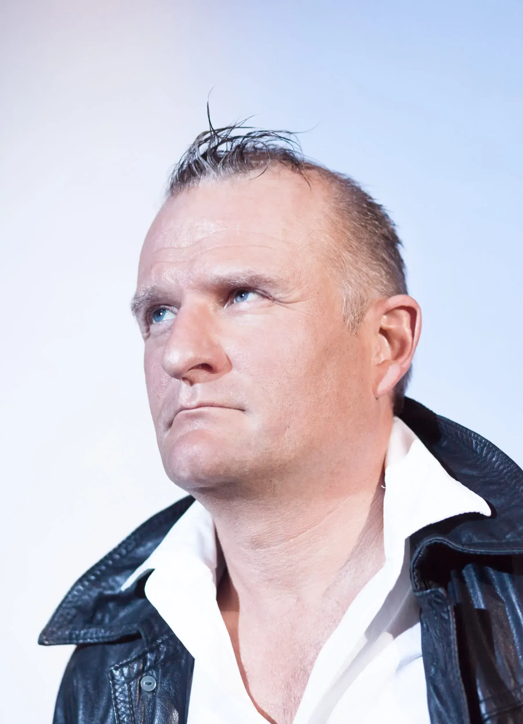 Portrait of Klaus Brömmelmeier in a leather jacket, looking upward against a pale background.