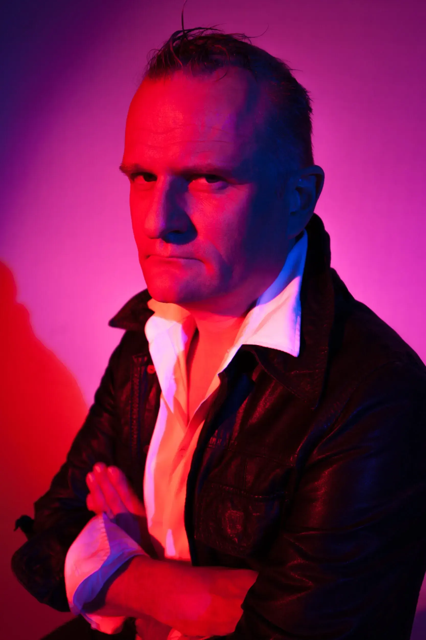 Portrait of Klaus Brömmelmeier with arms crossed, lit in pink and blue light.
