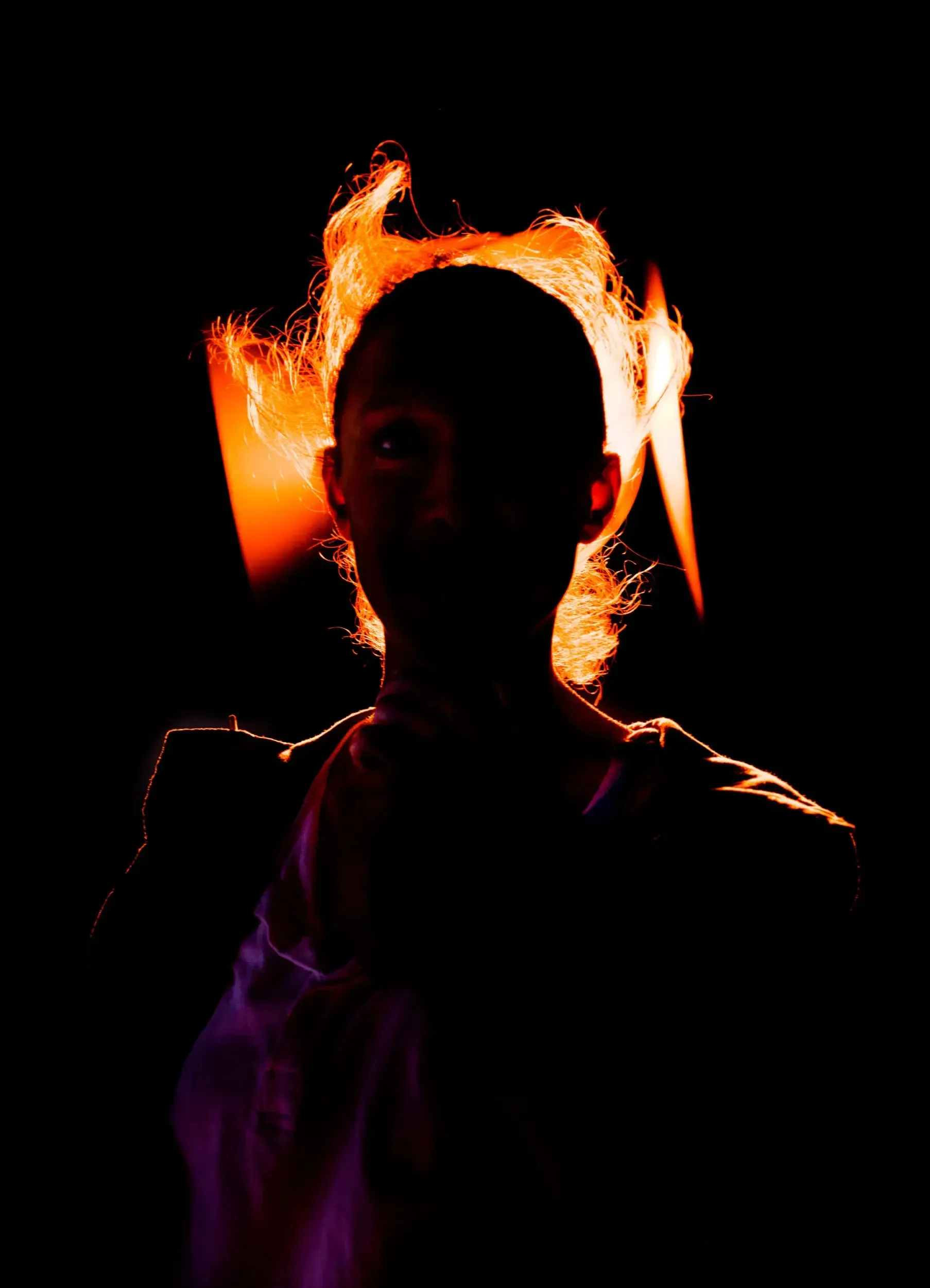 Silhouette portrait of Lena Schwarz with her hair rim-lit like flames against black.