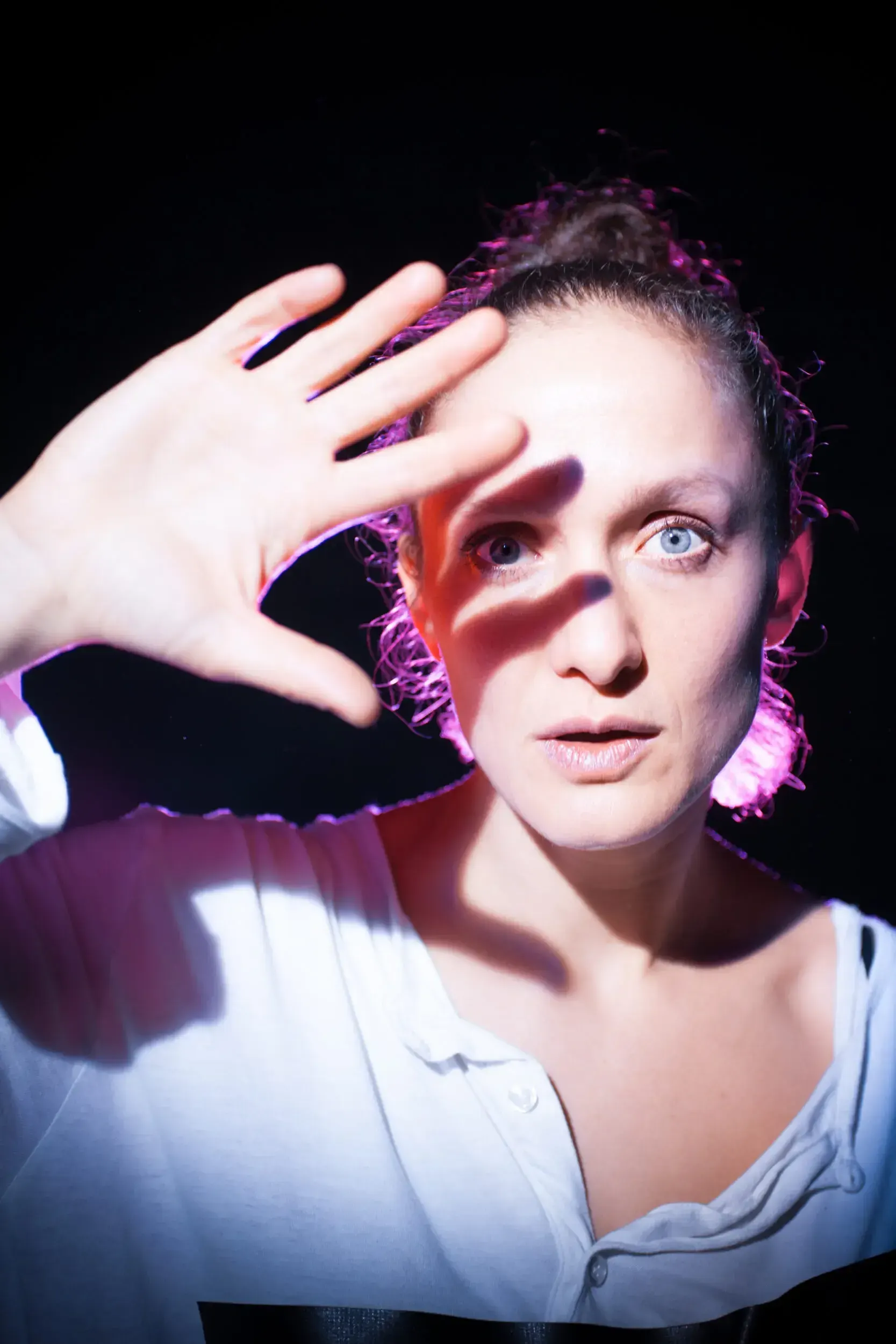 Portrait of Lena Schwarz raising a hand toward the camera, lit in pink and orange.
