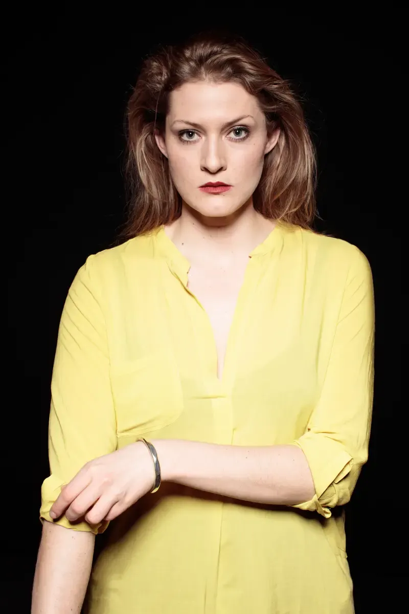 Portrait von Lisa-Katrina Mayer in gelber Bluse vor dunklem Hintergrund