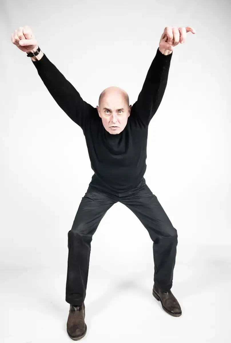 Studio portrait of actor Ludwig Boettger leaping with arms raised against a white background.