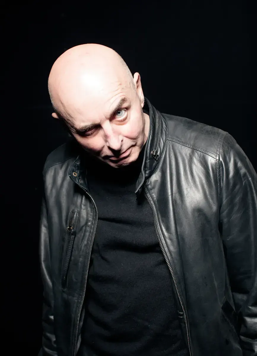 Portrait of actor Ludwig Boettger in a leather jacket, tilting his head with a wry expression against black.