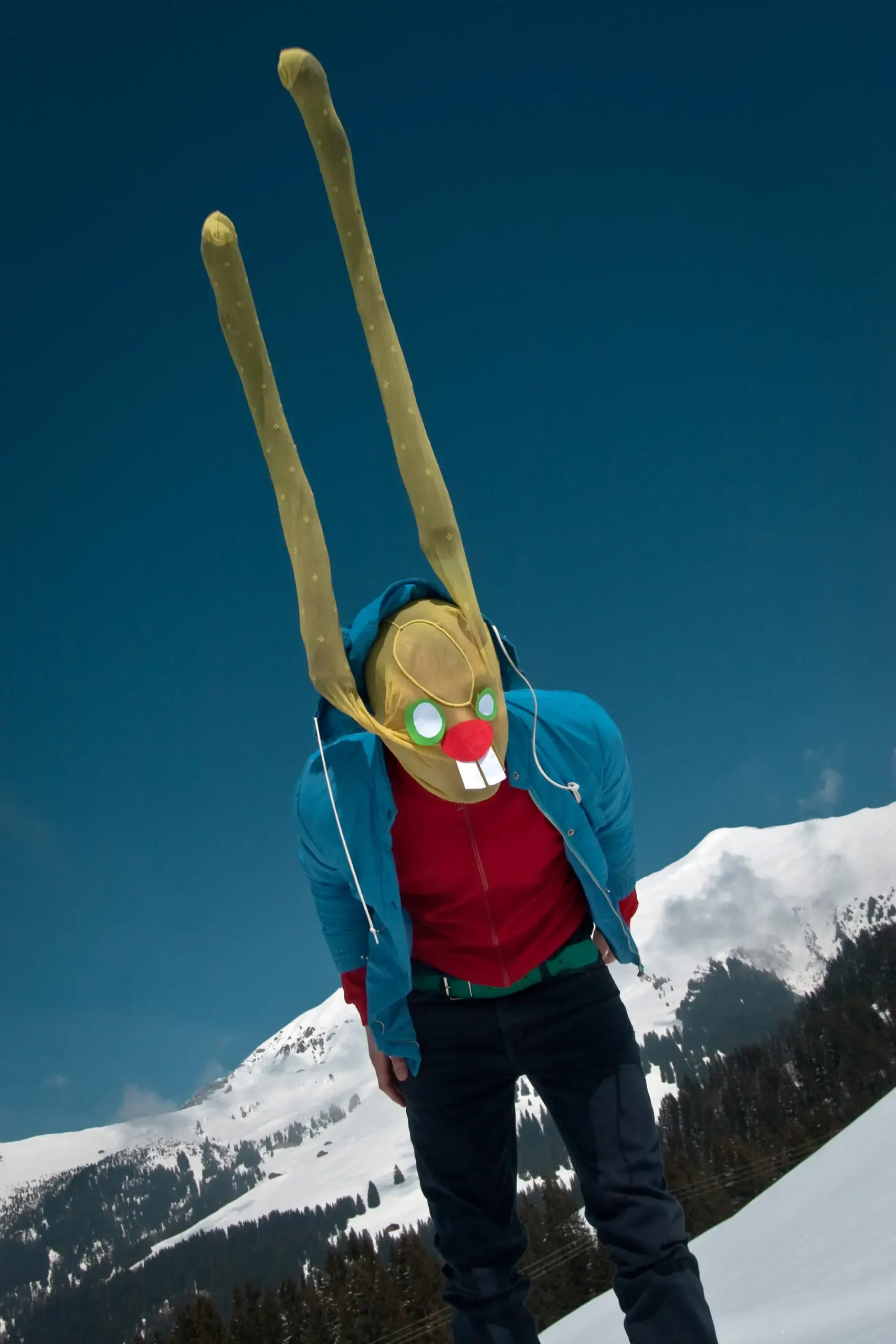 Person mit Hasenmaske und erhobenen Armen auf einem schneebedeckten Berg