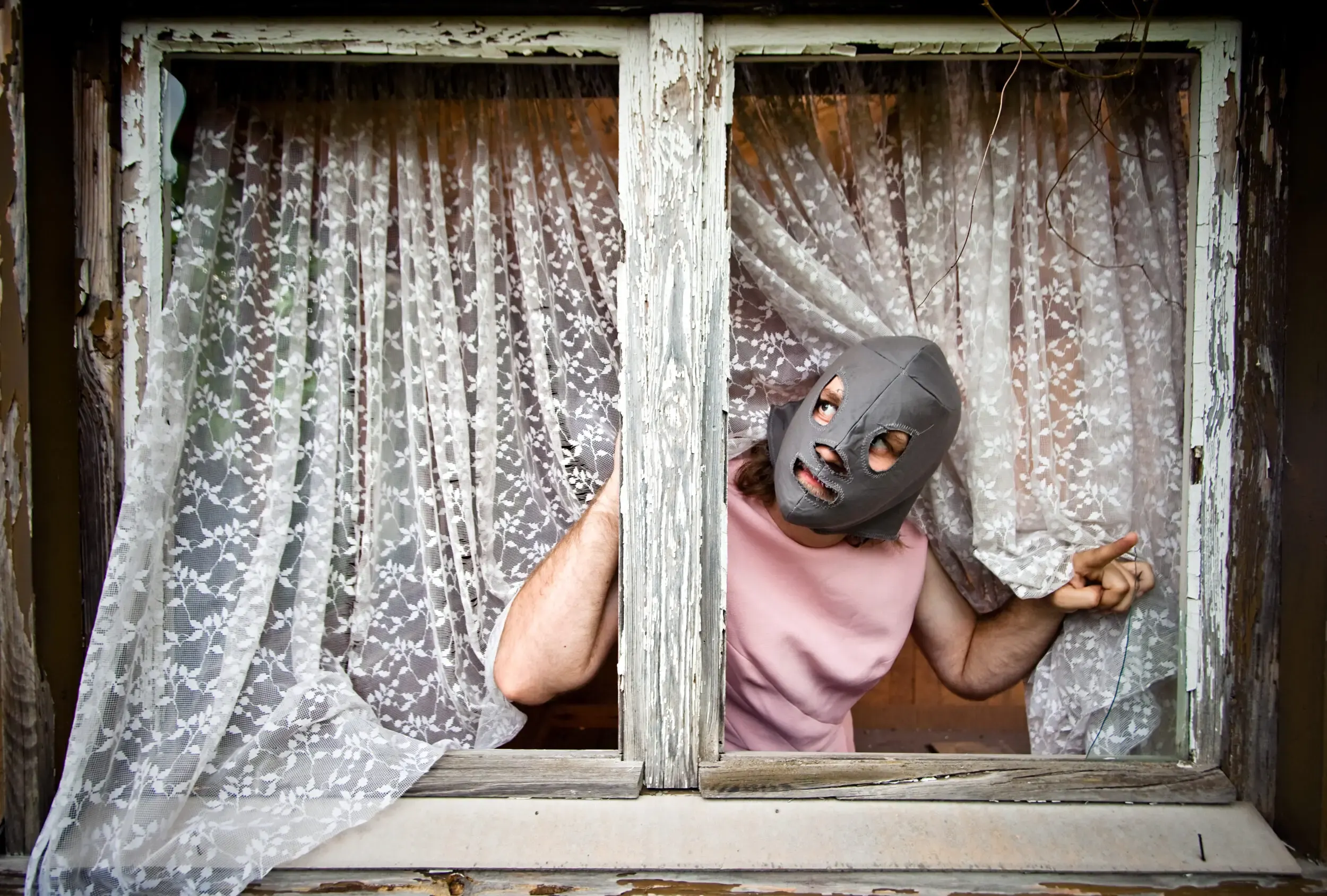 Person mit Tiermaske schaut durch einen Vorhang aus einem alten Fenster