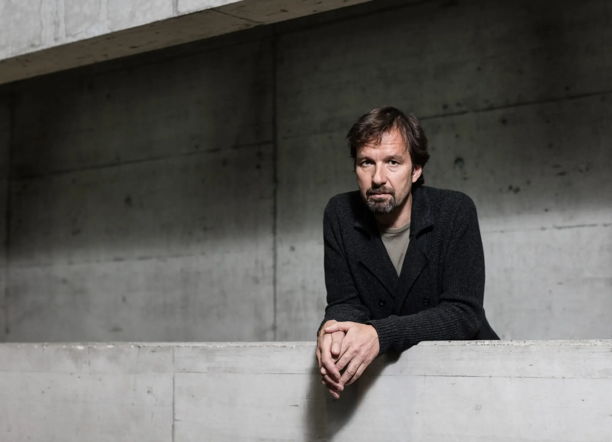 Michael Neuenschwander sitzt auf einer Betonmauer mit gefalteten Händen