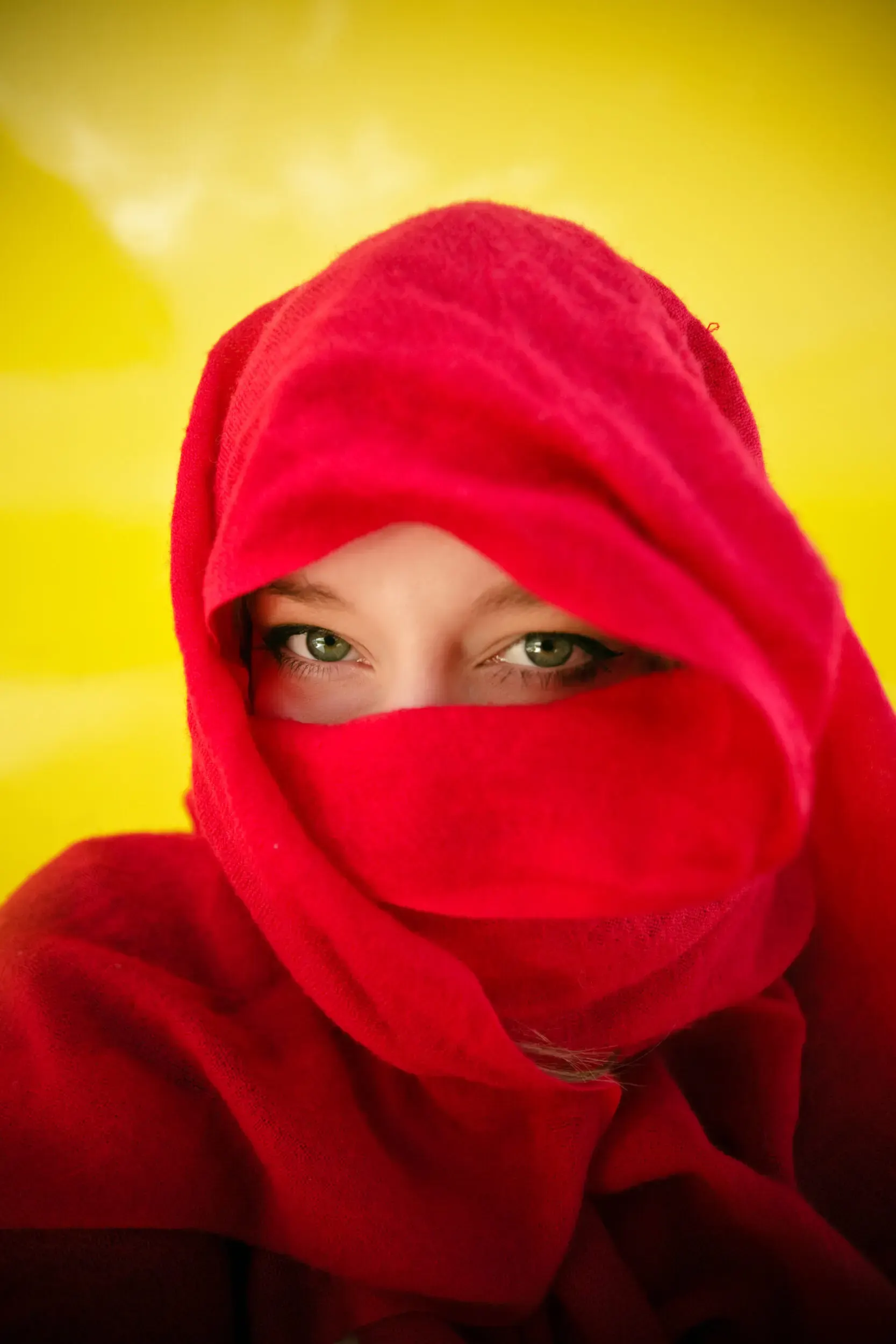 A person wearing a soft red scarf, partially covering their face, against a bright yellow background.