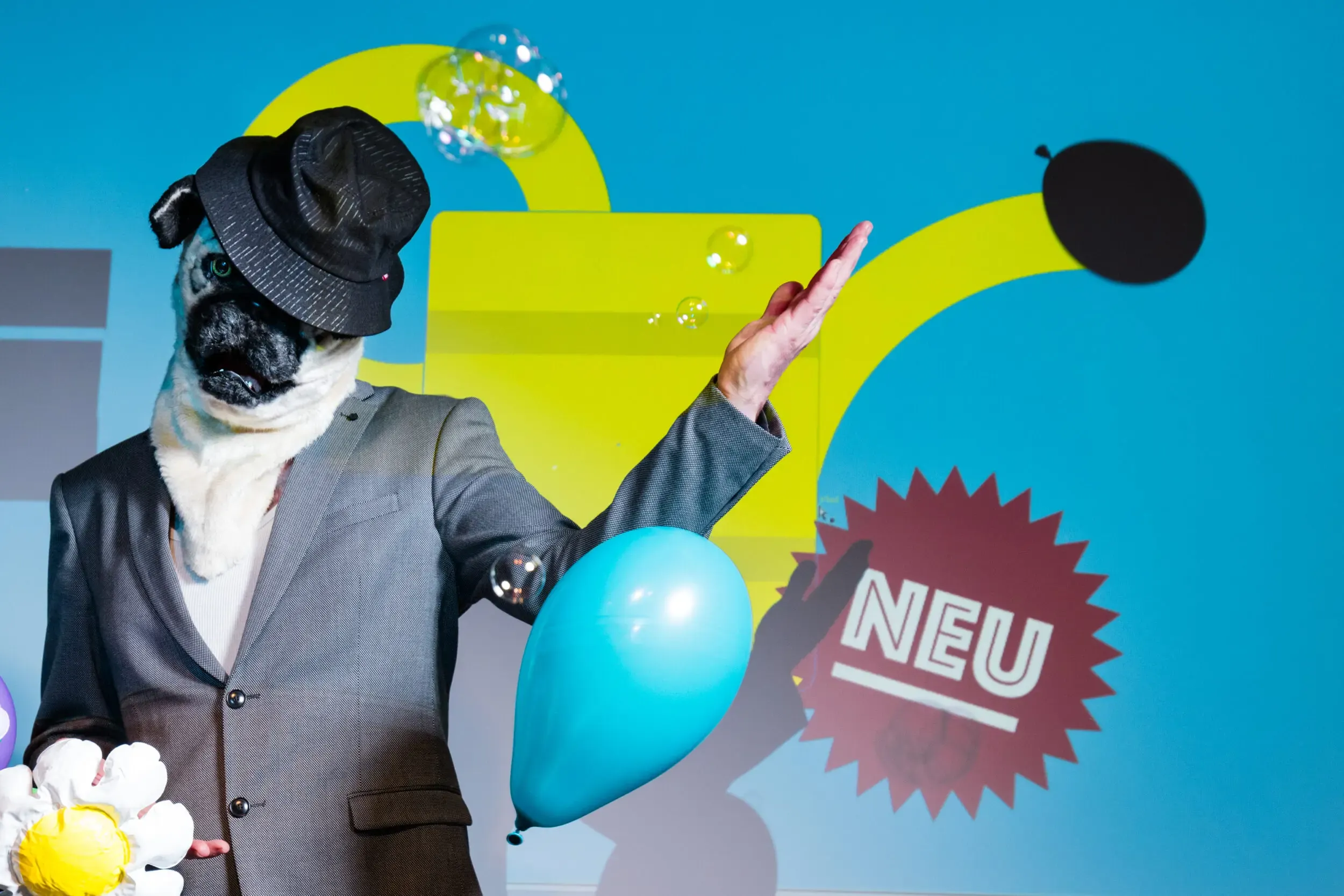 Person mit Gasmaske und projizierter gelber Grafik, „NEU“-Sticker