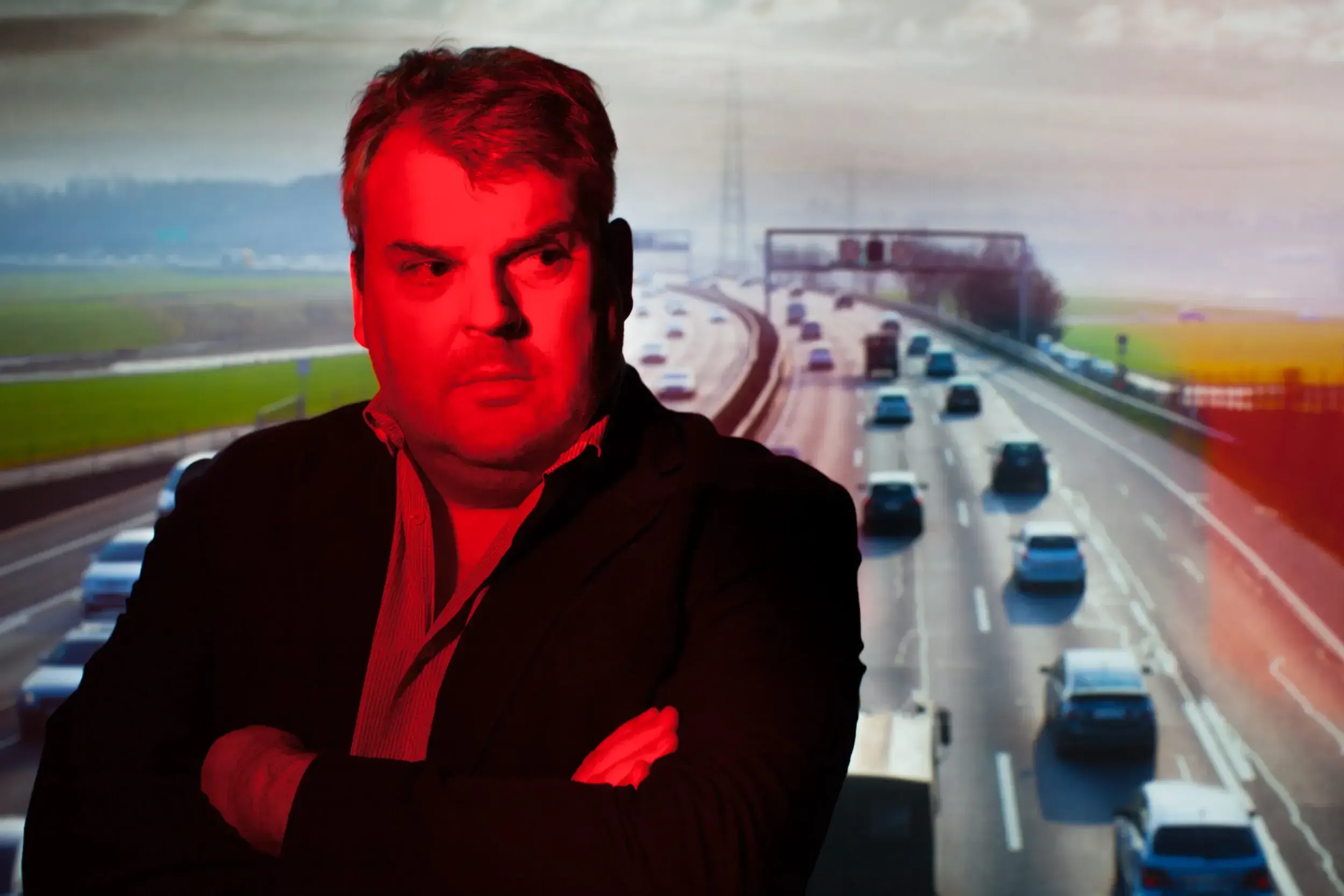 Red-toned photo composite of a man in a suit superimposed over a busy Swiss motorway, teaser image for the play 'A1 – Ein Stück Schweizer Strasse'.