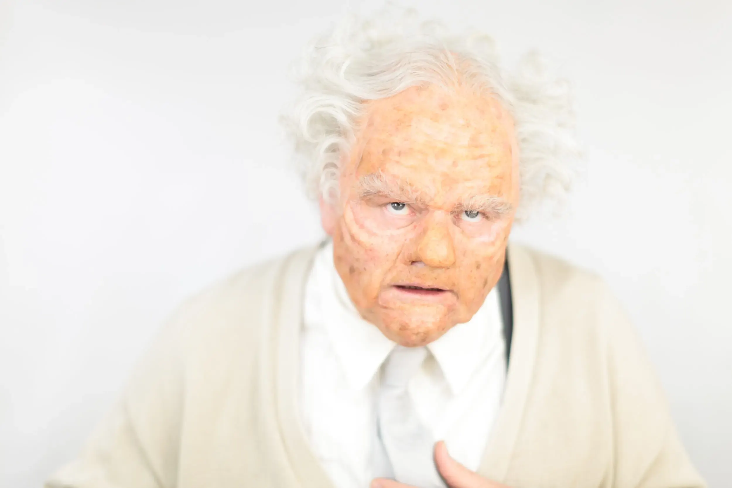 Älterer Mann mit weissem Haar und überraschtem Gesichtsausdruck vor weissem Hintergrund