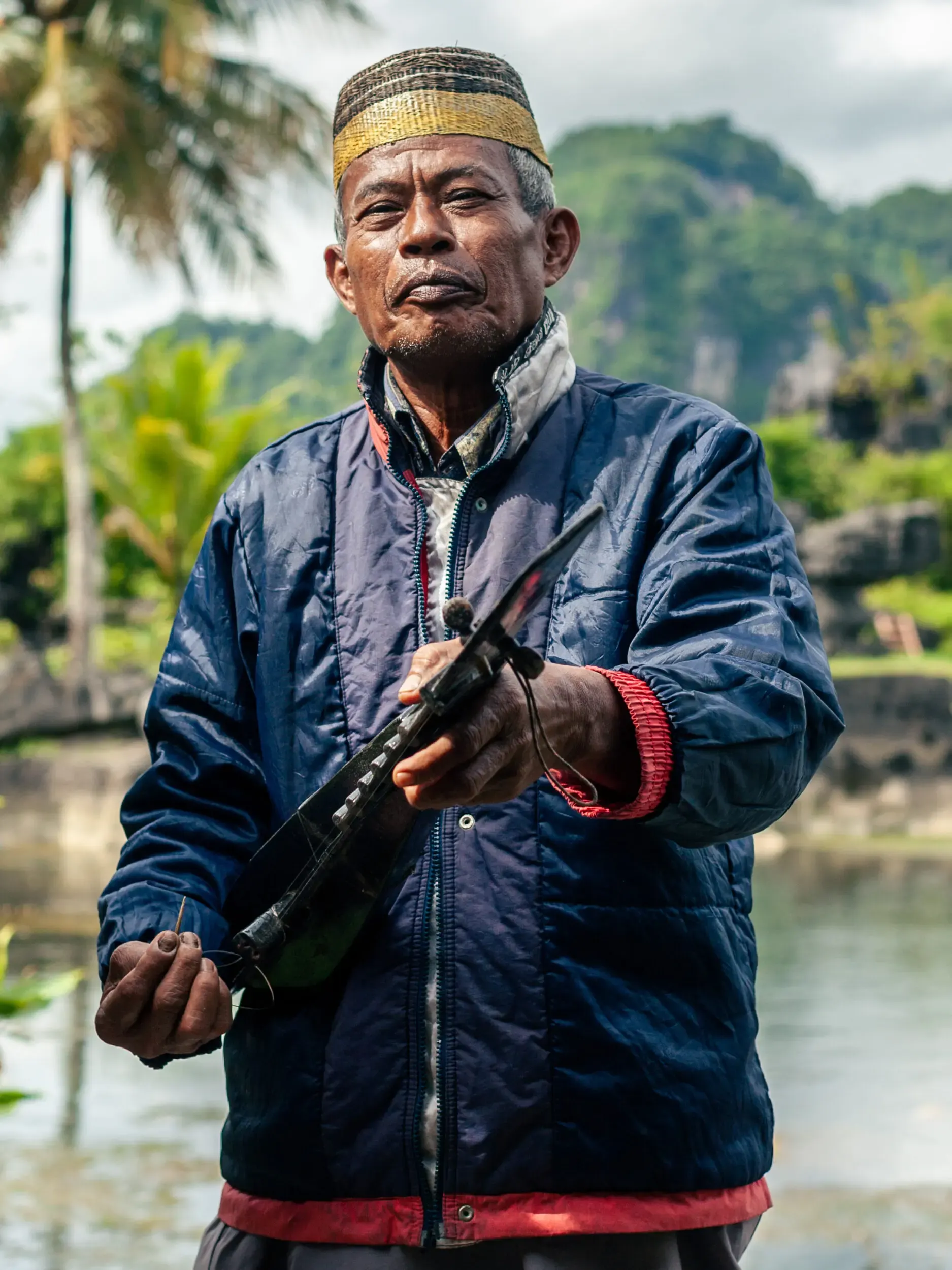Älterer Mann mit traditioneller Kopfbedeckung am Flussufer, Sulawesi