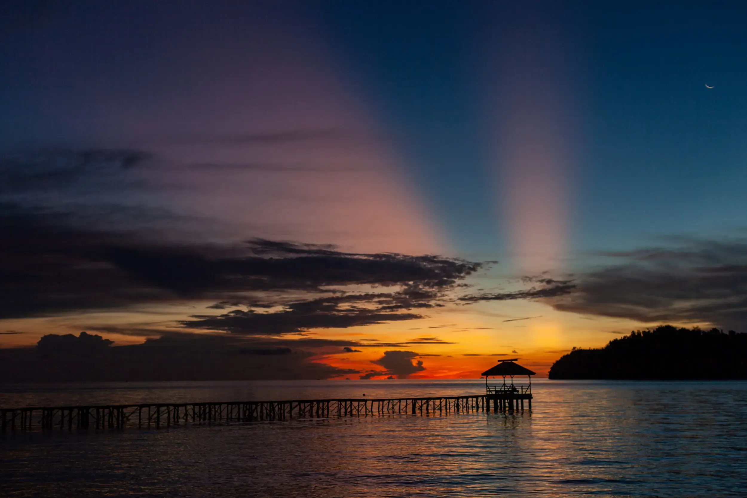 Sonnenuntergang über dem Meer mit Stegsilhouette, Sulawesi