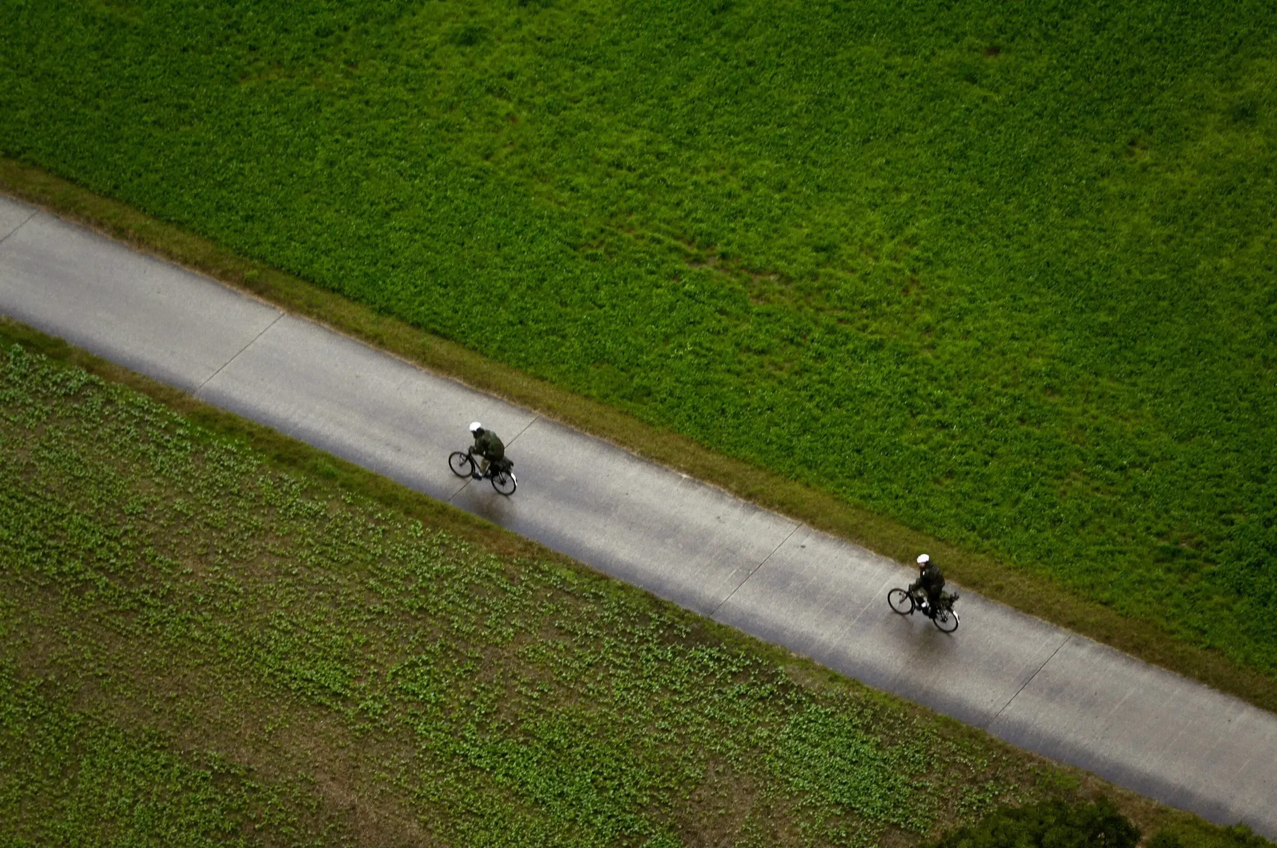 Aerial view of two soldiers cycling along a road between green fields during a Swiss Raid Command exercise.