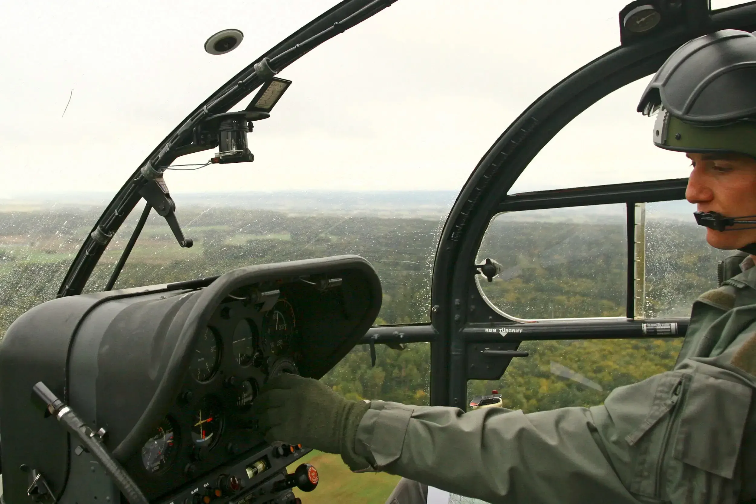View from inside a helicopter cockpit over forested hills during a Swiss Raid Command flight.