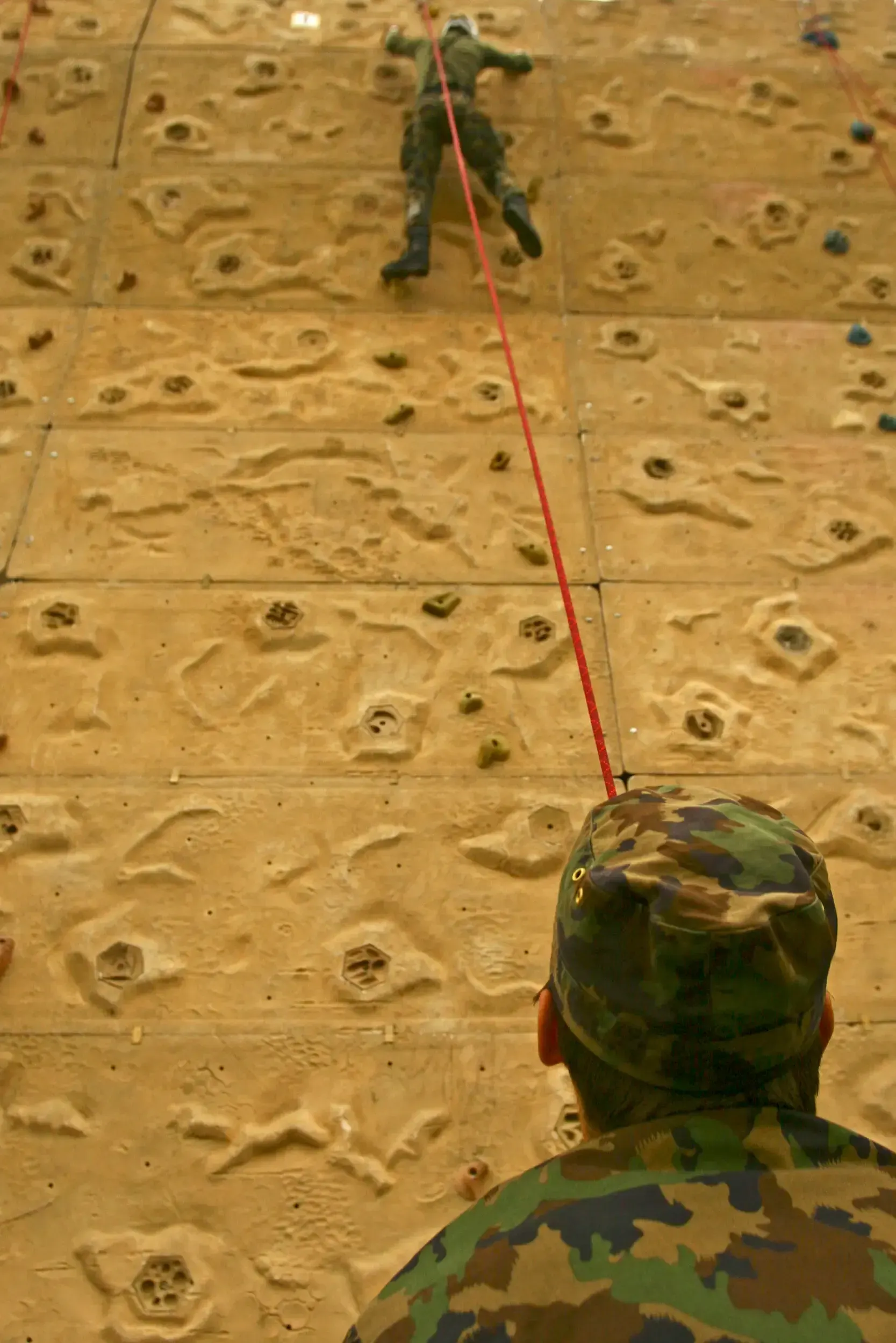 Soldier belaying a climber on an indoor climbing wall during training.