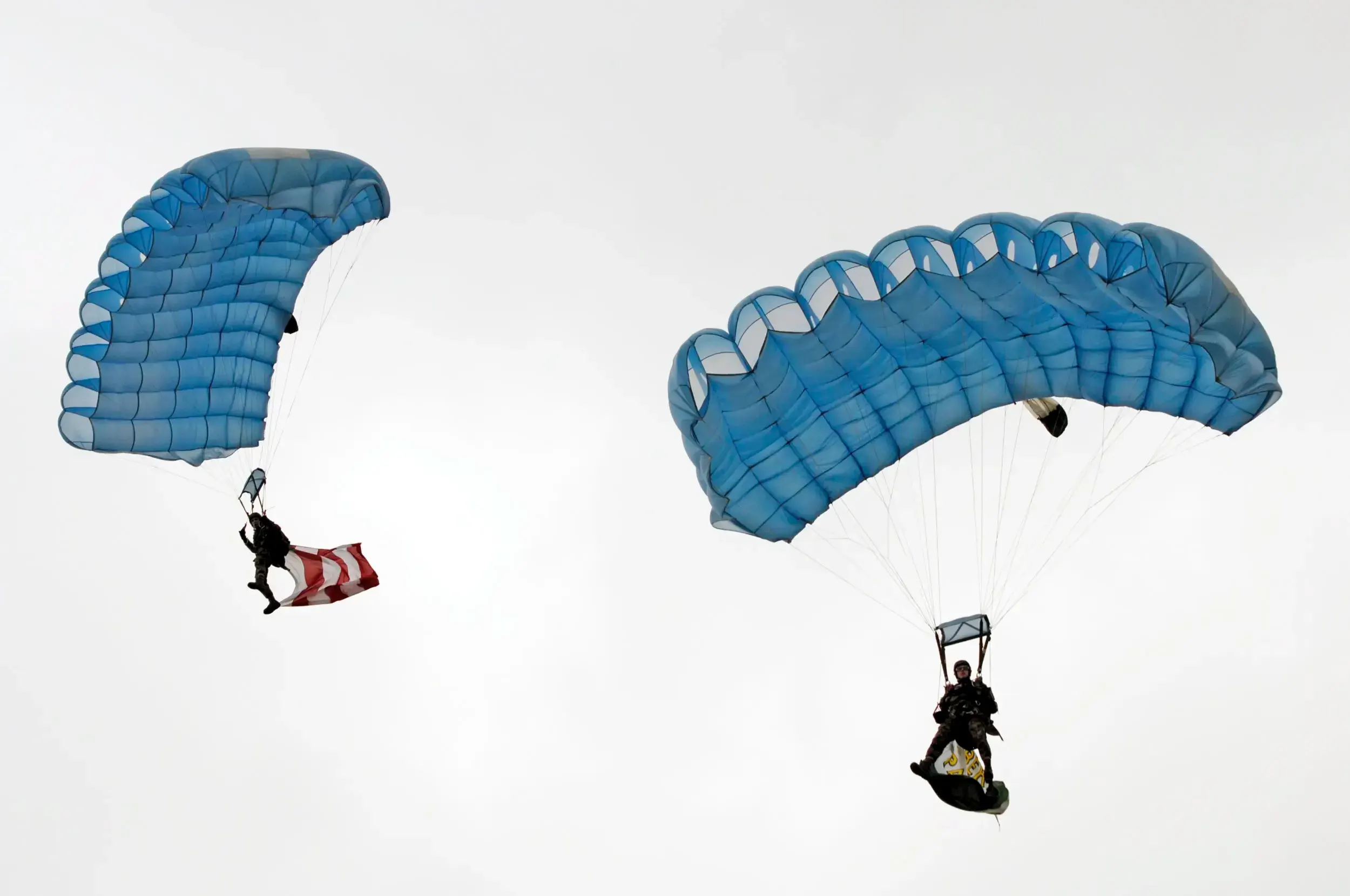 Two parachutists descending with blue canopies, one carrying a red and white flag.