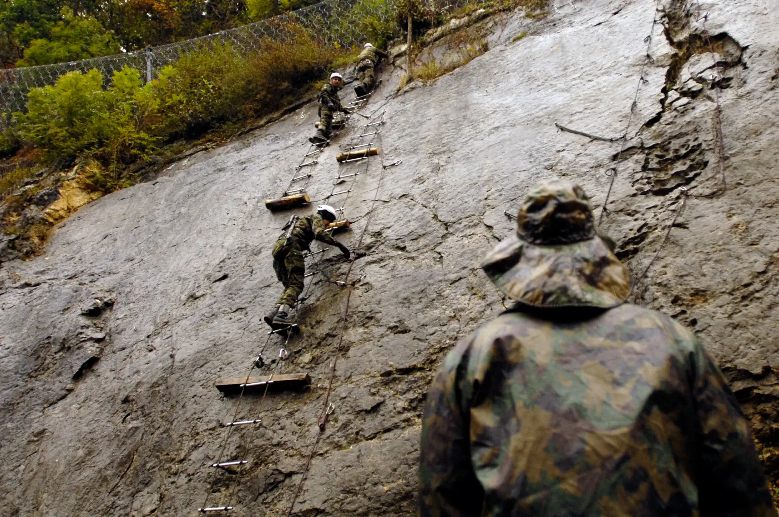 Soldiers climbing a rope ladder up a rock face during a Swiss Raid Command training exercise.
