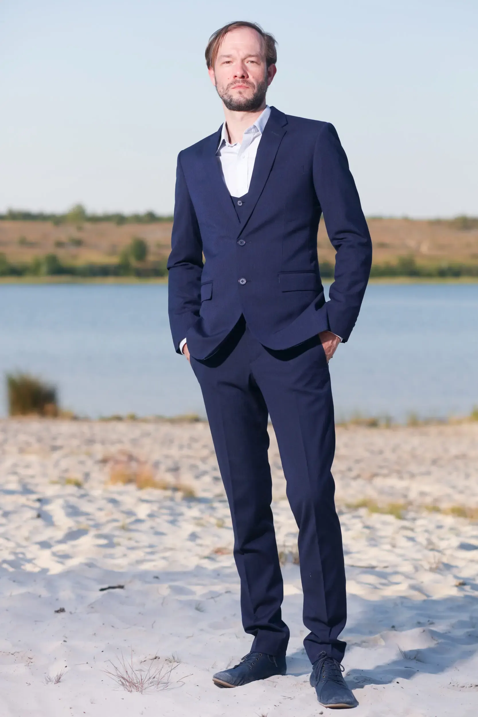 Tim Wildner steht im Anzug am Strand