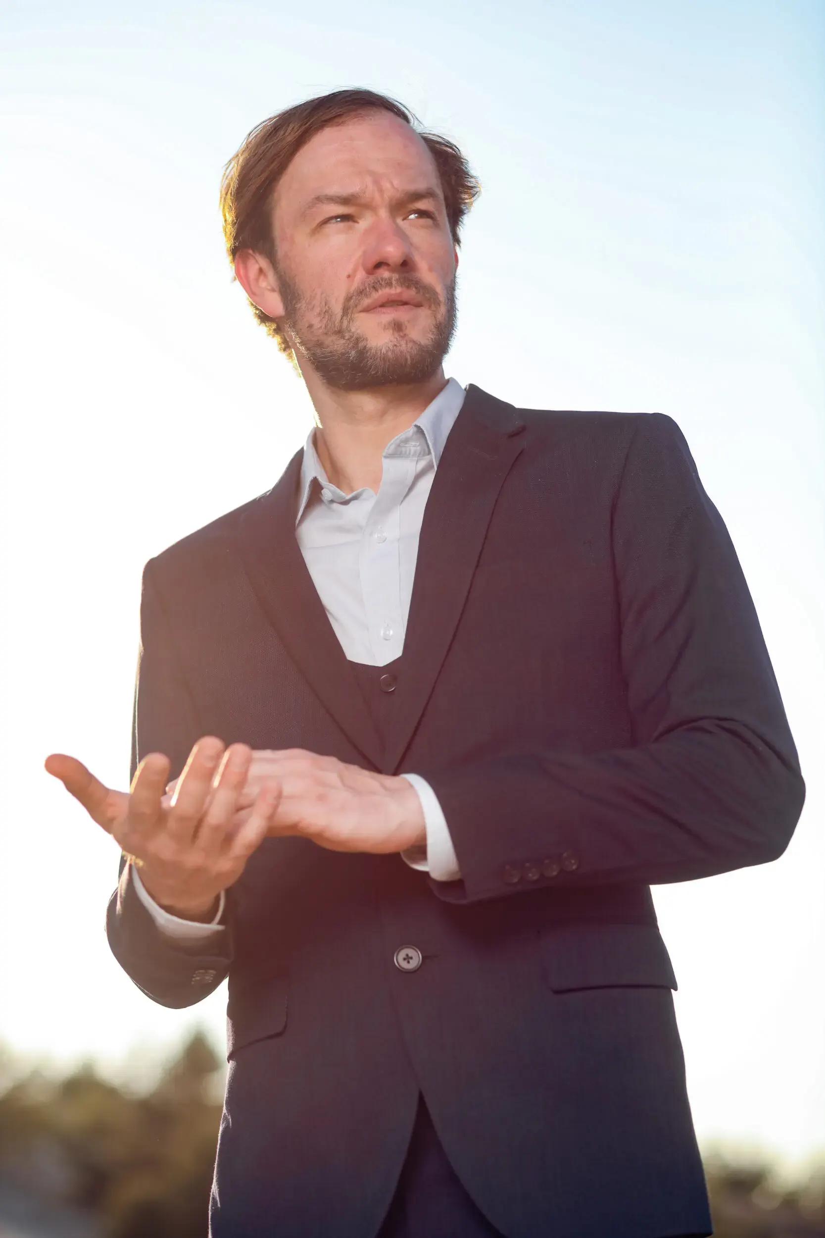 Tim Wildner gestikuliert im Anzug vor blauem Himmel